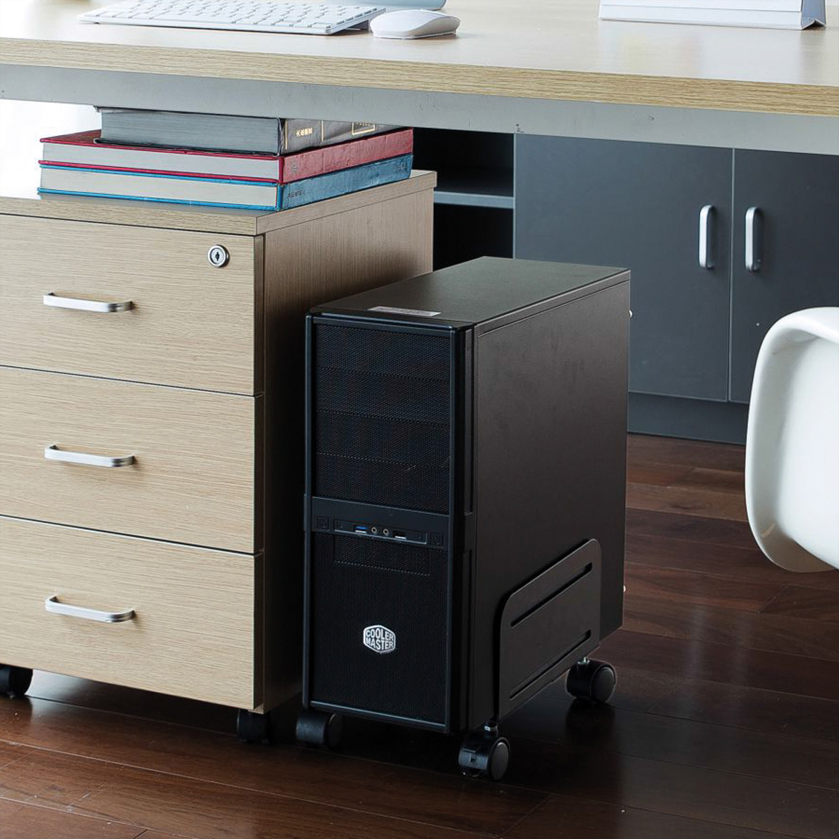 Schwarzer Computer Tower auf Rädern neben Holzschrank und Schreibtisch.