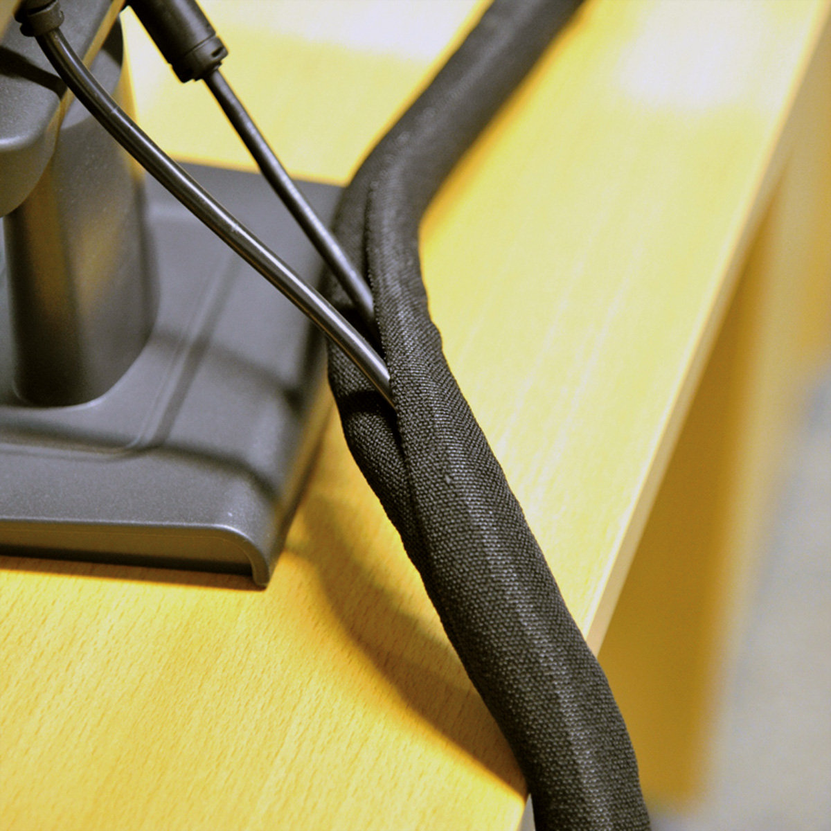 Zwarte kabel in geweven huls op gele tafel, met monitorstandaardvoet.