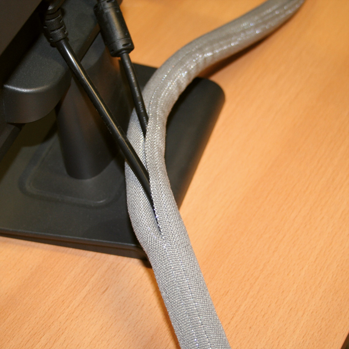 Primo piano di cavi e di un manicotto intrecciato grigio, il tutto su un tavolo di legno. Supporto monitor nero sullo sfondo.
