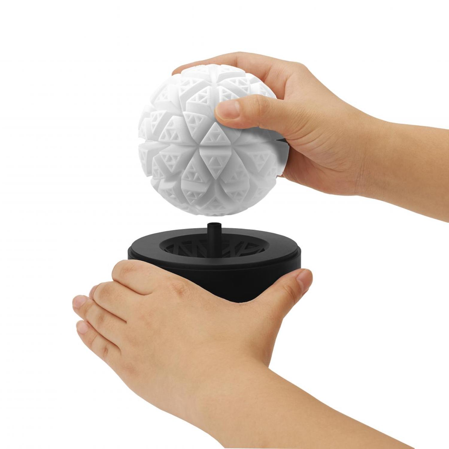 Hände halten einen weißen Ball und setzen ihn in eine schwarze Basis ein. Der Ball hat Dreieckschnitte.