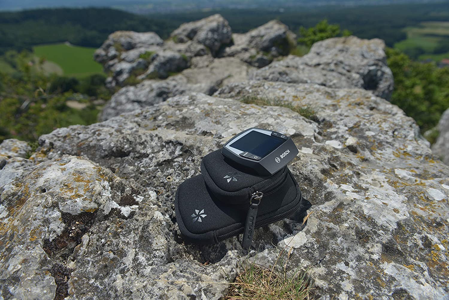 Ein GPS-Gerät und Beutel auf felsigem Untergrund, mit verschwommenem Naturhintergrund.