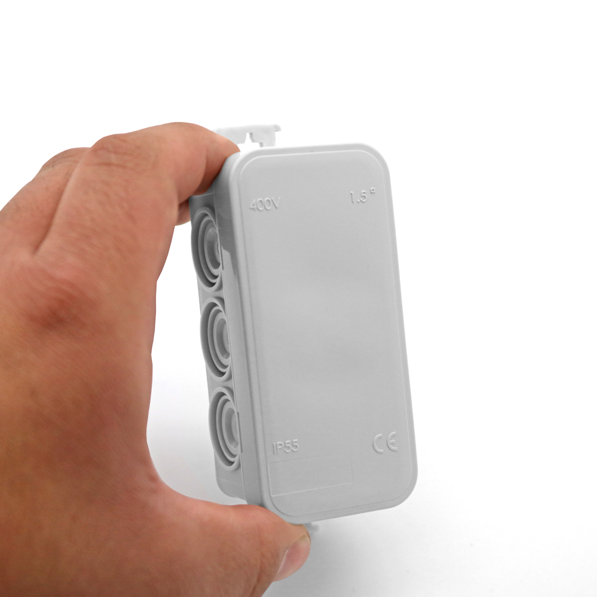 Eine Hand hält eine graue elektrische Verteilerdose vor einer weißen Wand.