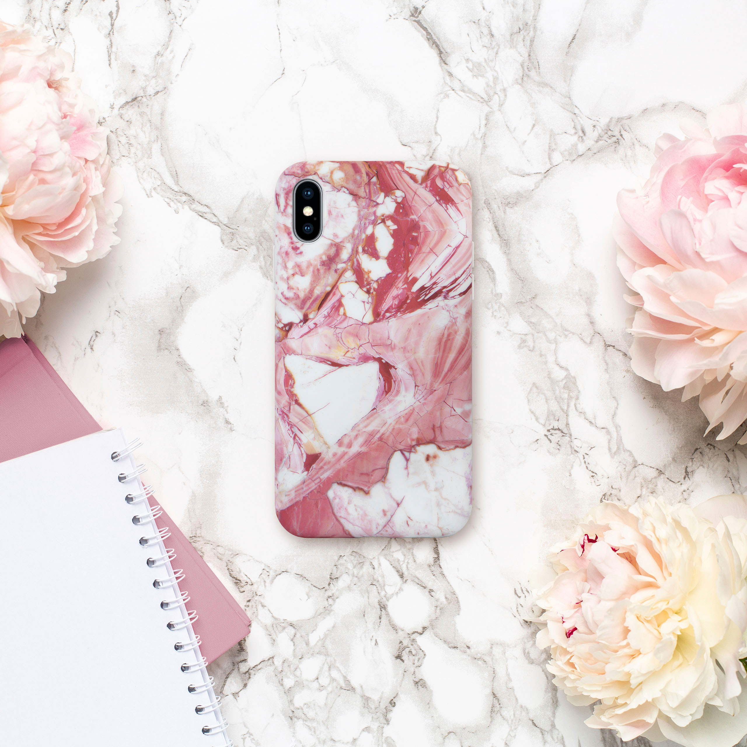 Rosa-weiße Marmor-Handyhülle, umgeben von rosa Pfingstrosen und Notizbüchern.