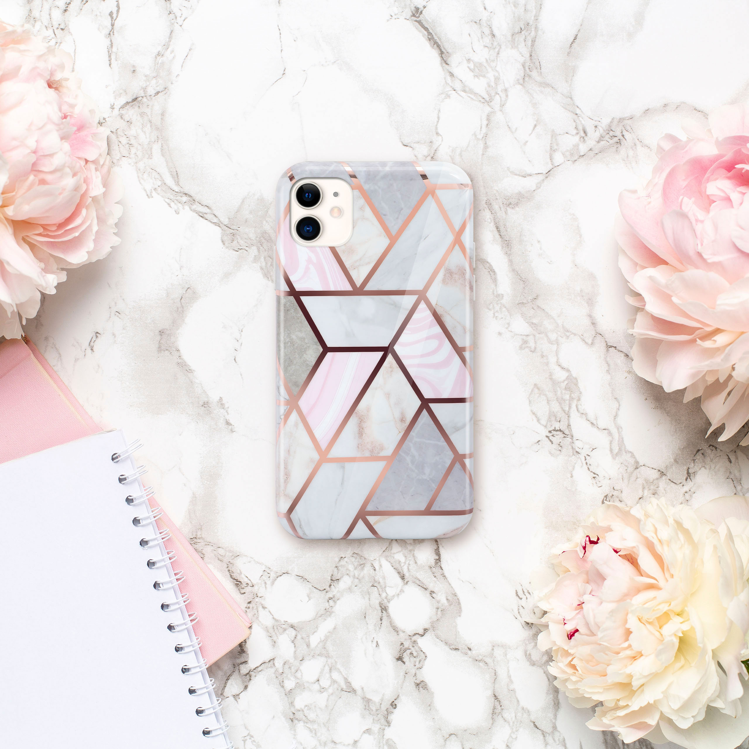 Handyhülle mit Marmor- und geometrischem Design. Rosa und graue Muster. Umgebung sind rosa Blumen und Notizbücher.