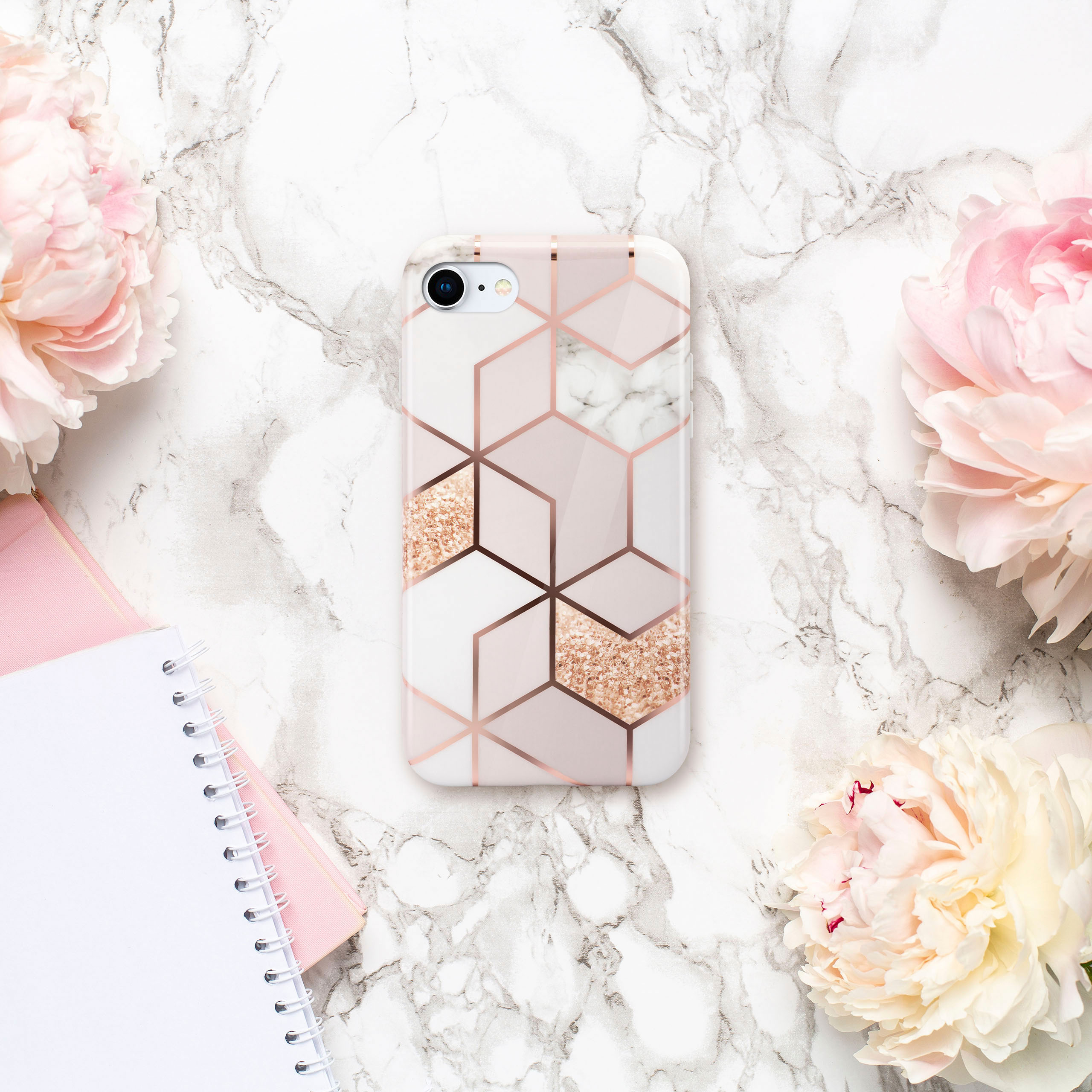 Handyhülle mit geometrischem Roségold-Design auf Marmorhintergrund mit rosa Pfingstrosen und einem Notizbuch.