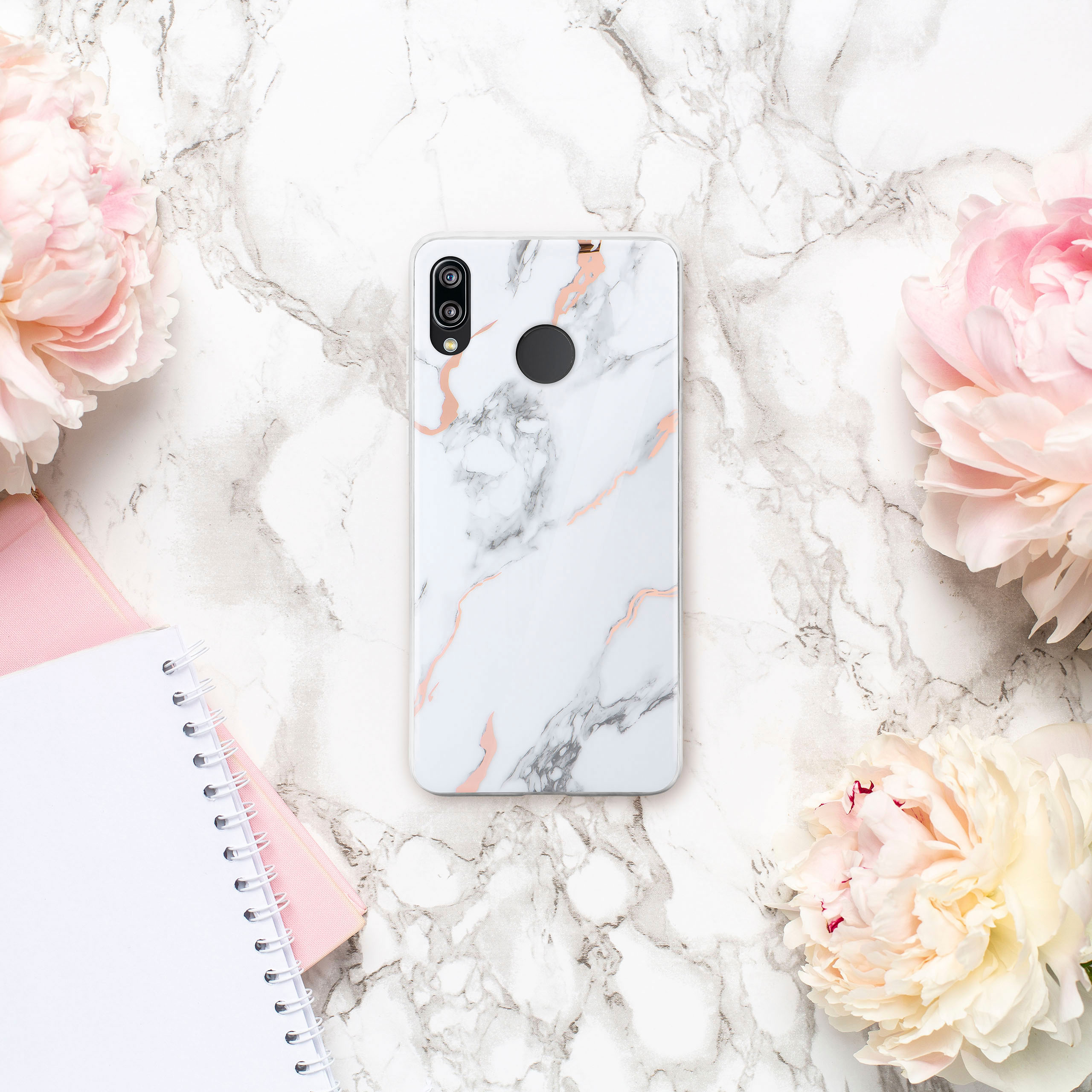 Handyhülle mit Marmordesign auf Marmorhintergrund mit Blumen und Notizblock.
