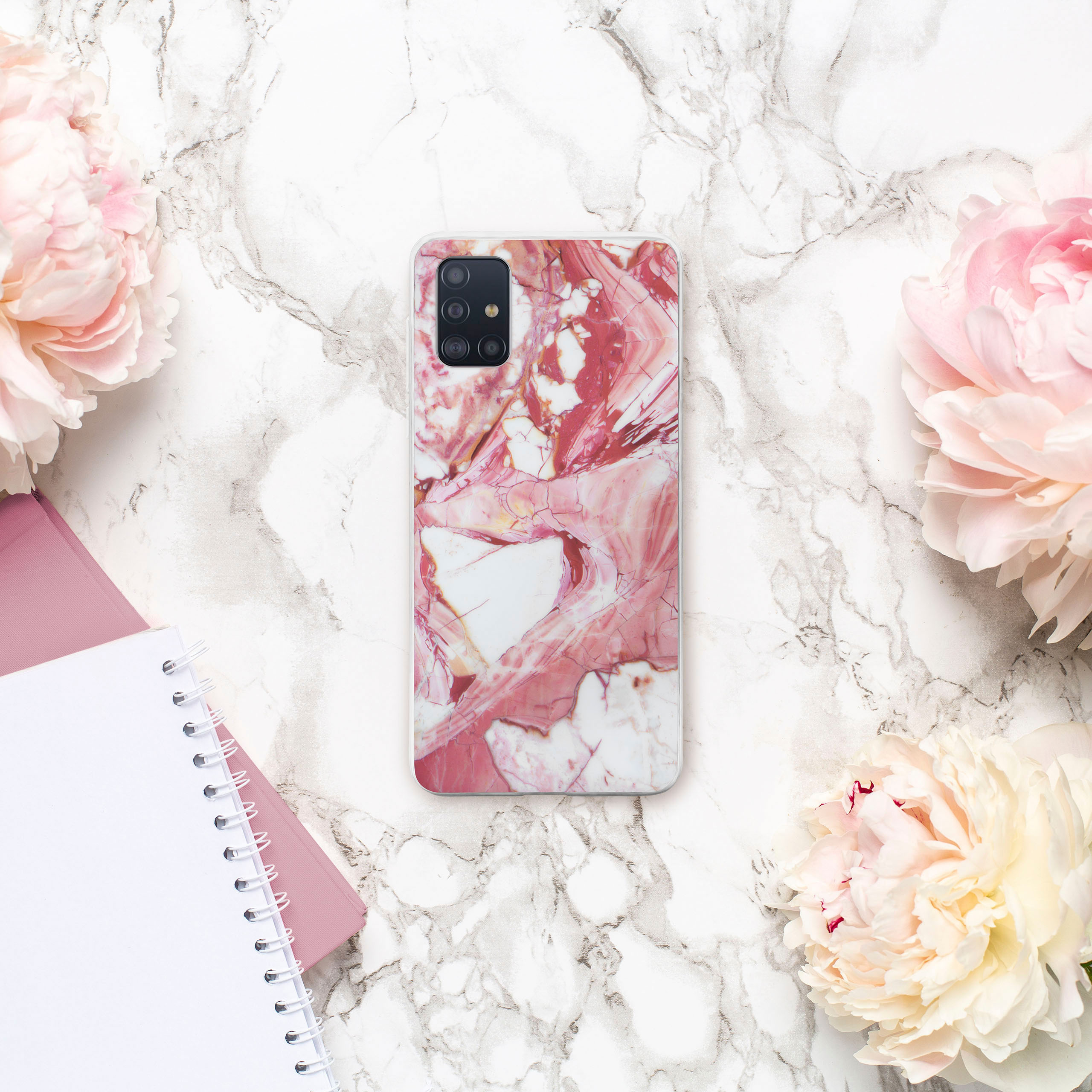 Handyhülle auf Marmoroberfläche mit rosa Pfingstrosen und einem Notizbuch. Rosa-weiße Marmorhülle.