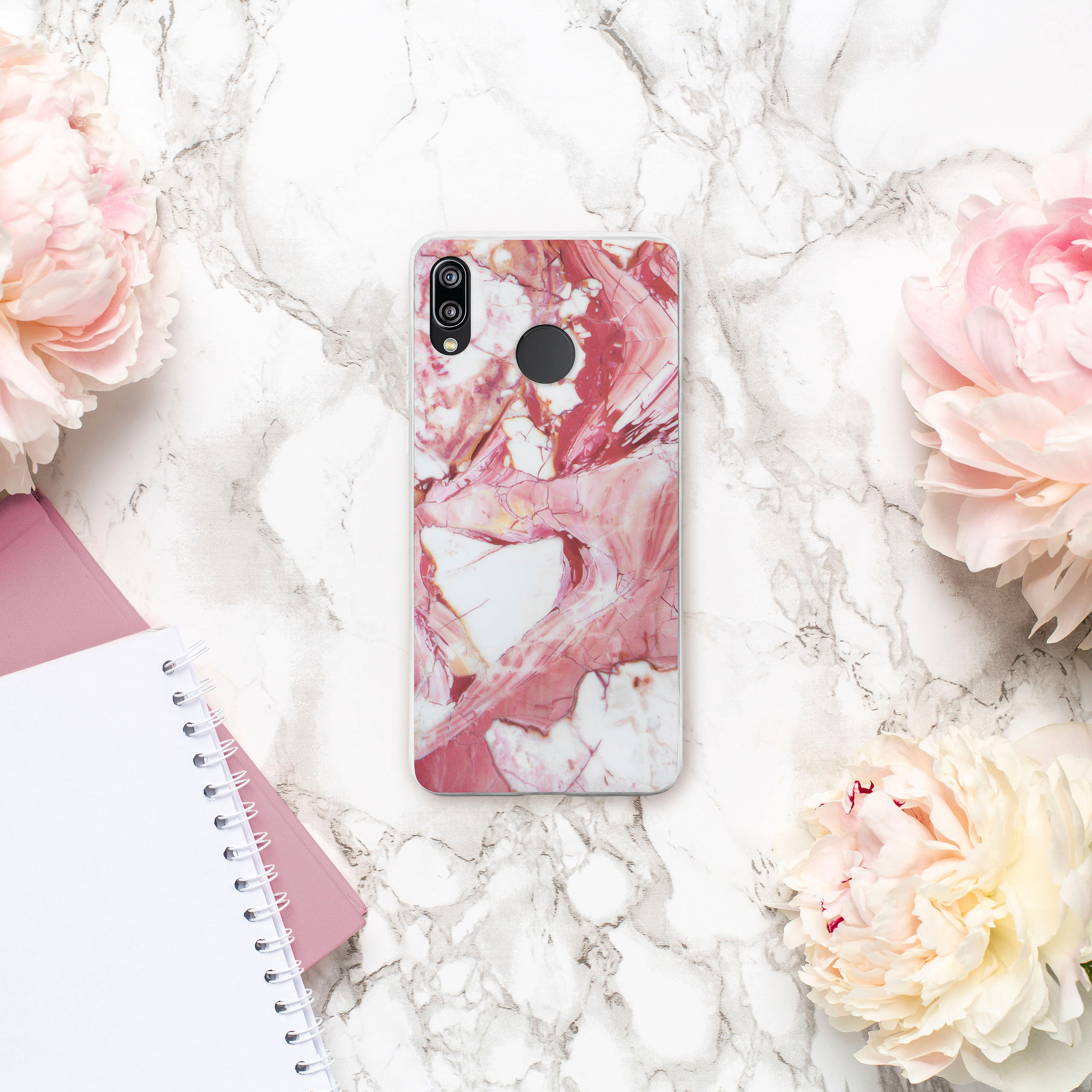 Handyhülle auf Marmoroberfläche mit rosa Pfingstrosen und Notizbuch. Hülle hat rosa und weißes Marmor-Design.