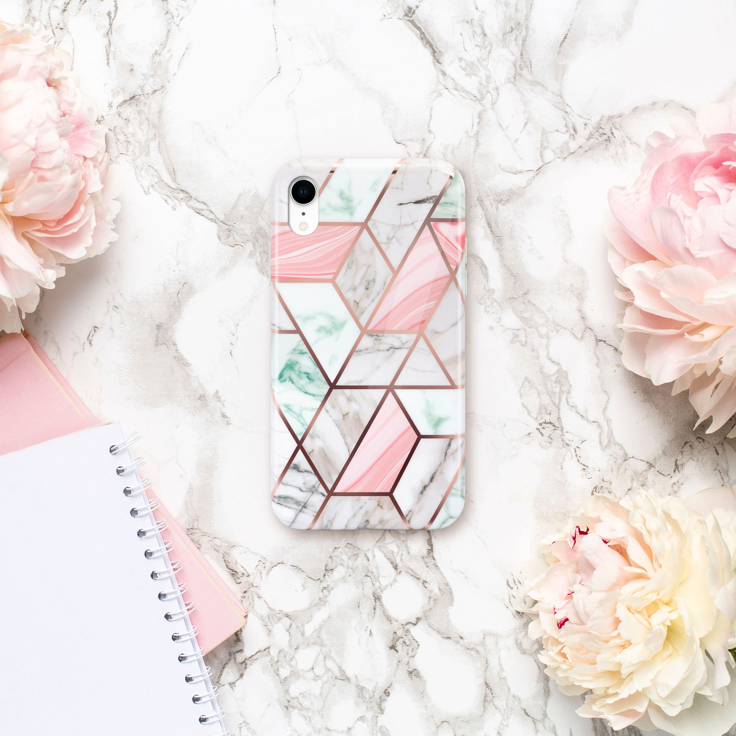 Handyhülle mit rosa und marmornem geometrischem Design, umgeben von Pfingstrosen und Notizblock.