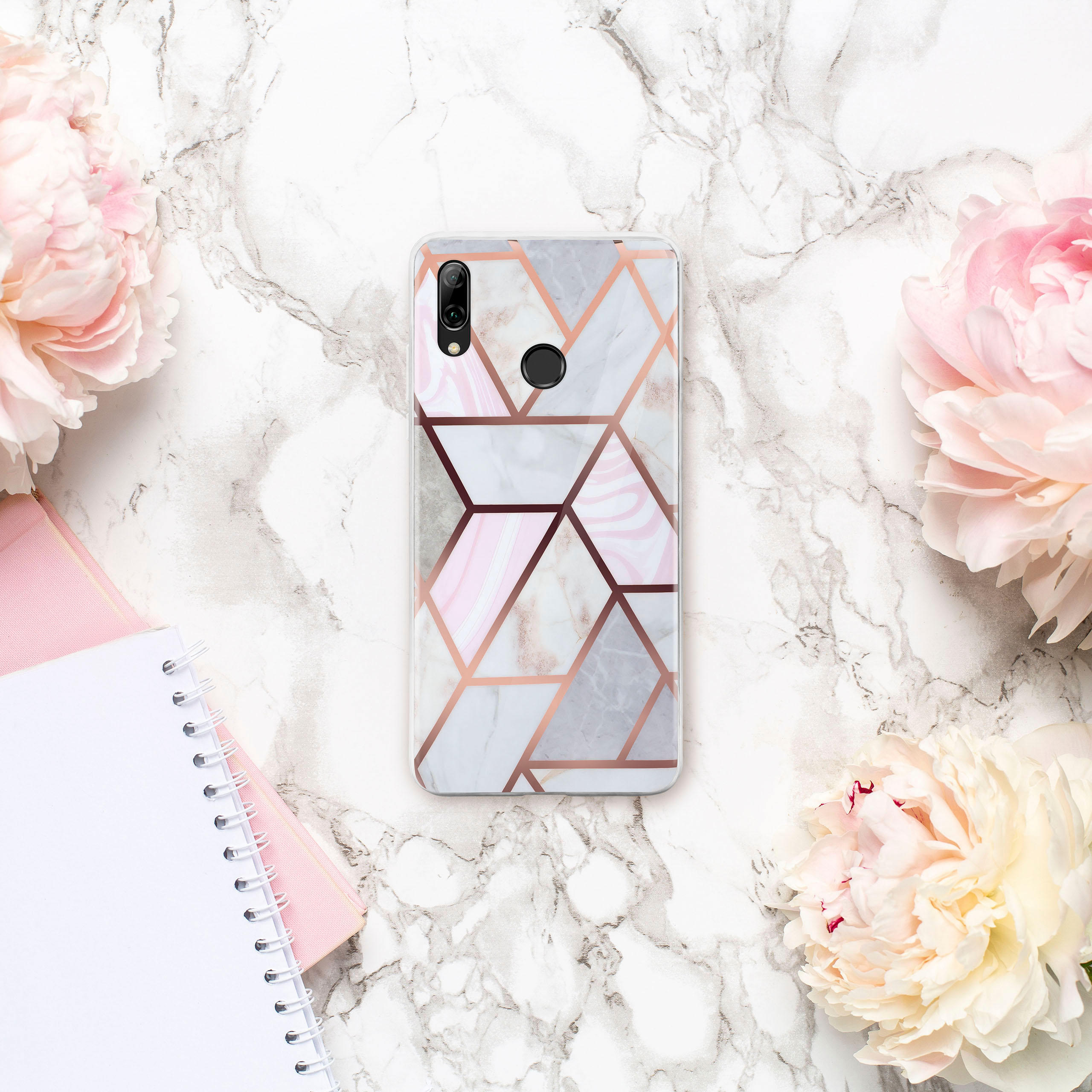 Handyhülle mit geometrischem Design auf Marmoroberfläche, umgeben von Blumen und Notizbuch.