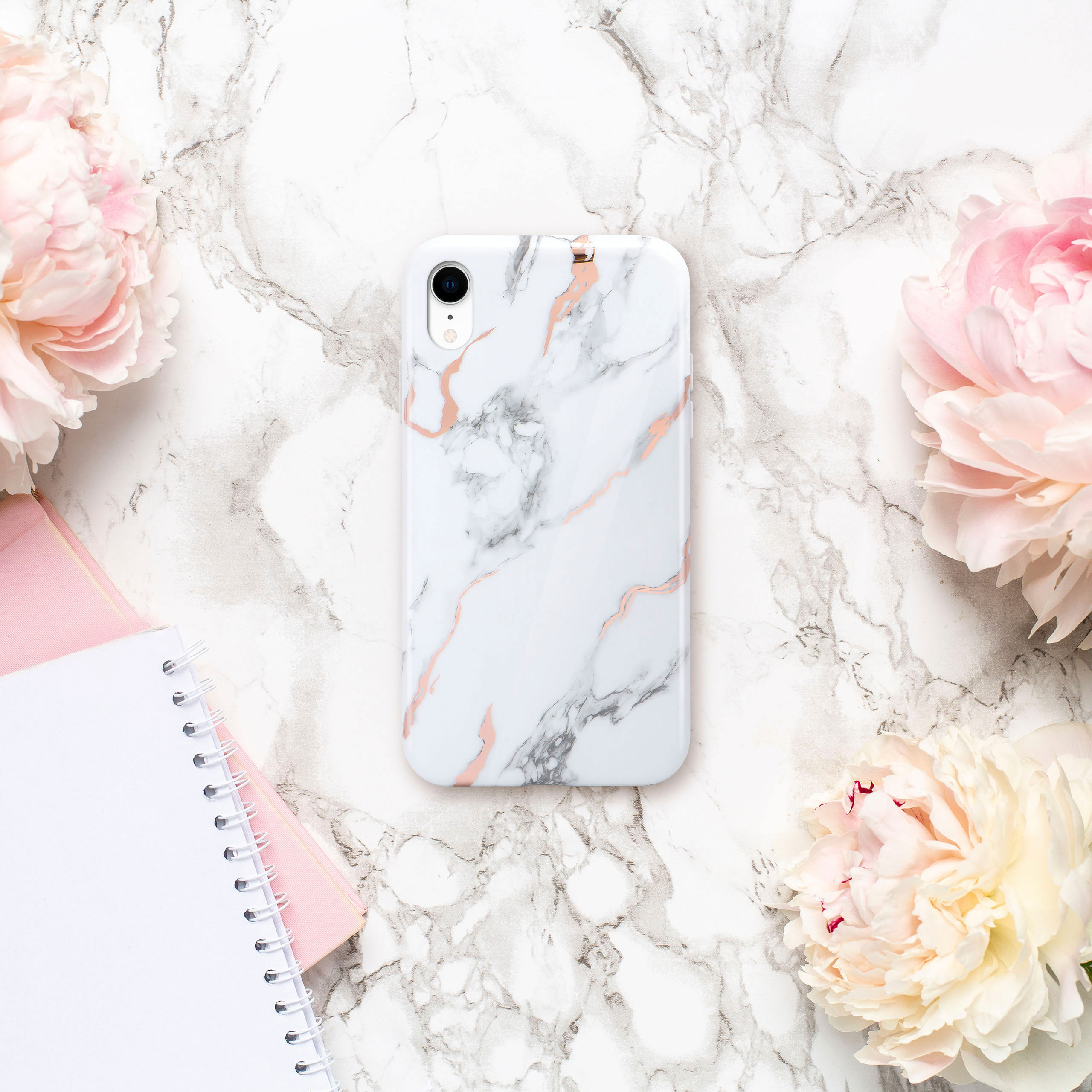 Weißes Marmor-Handy-Case mit rosa Akzenten, umgeben von Pfingstrosen und einem Notizblock.