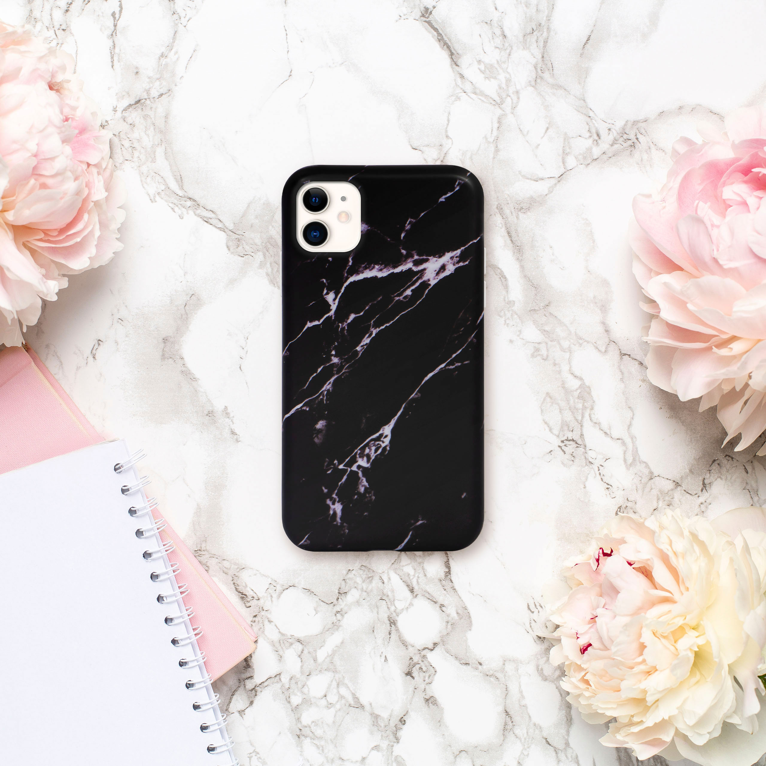 Schwarze Handyhülle mit Marmordesign, umgeben von Blumen und einem Notizbuch.