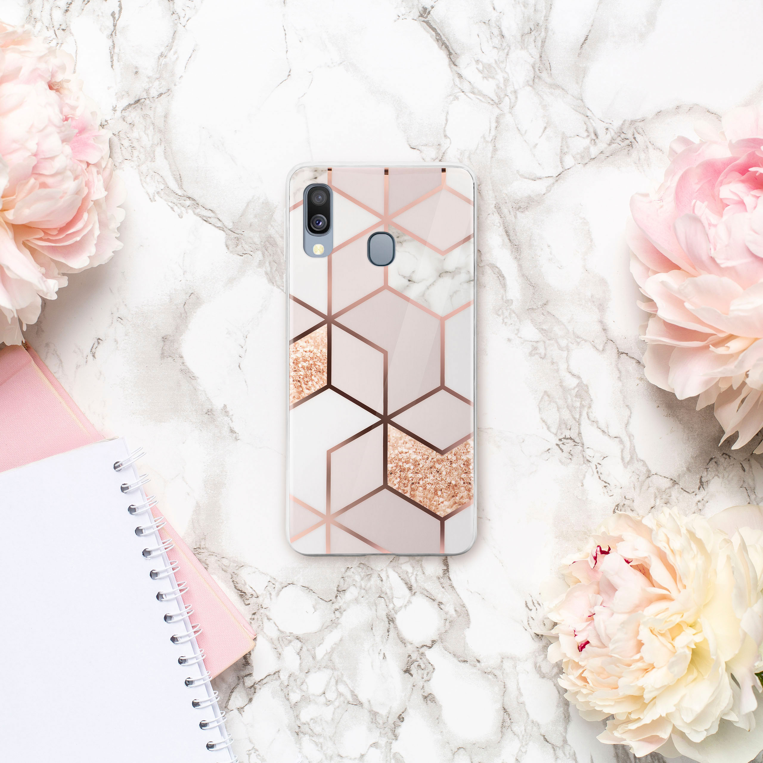 Handyhülle auf Marmorhintergrund, mit rosa Blumen und einem Notizbuch.