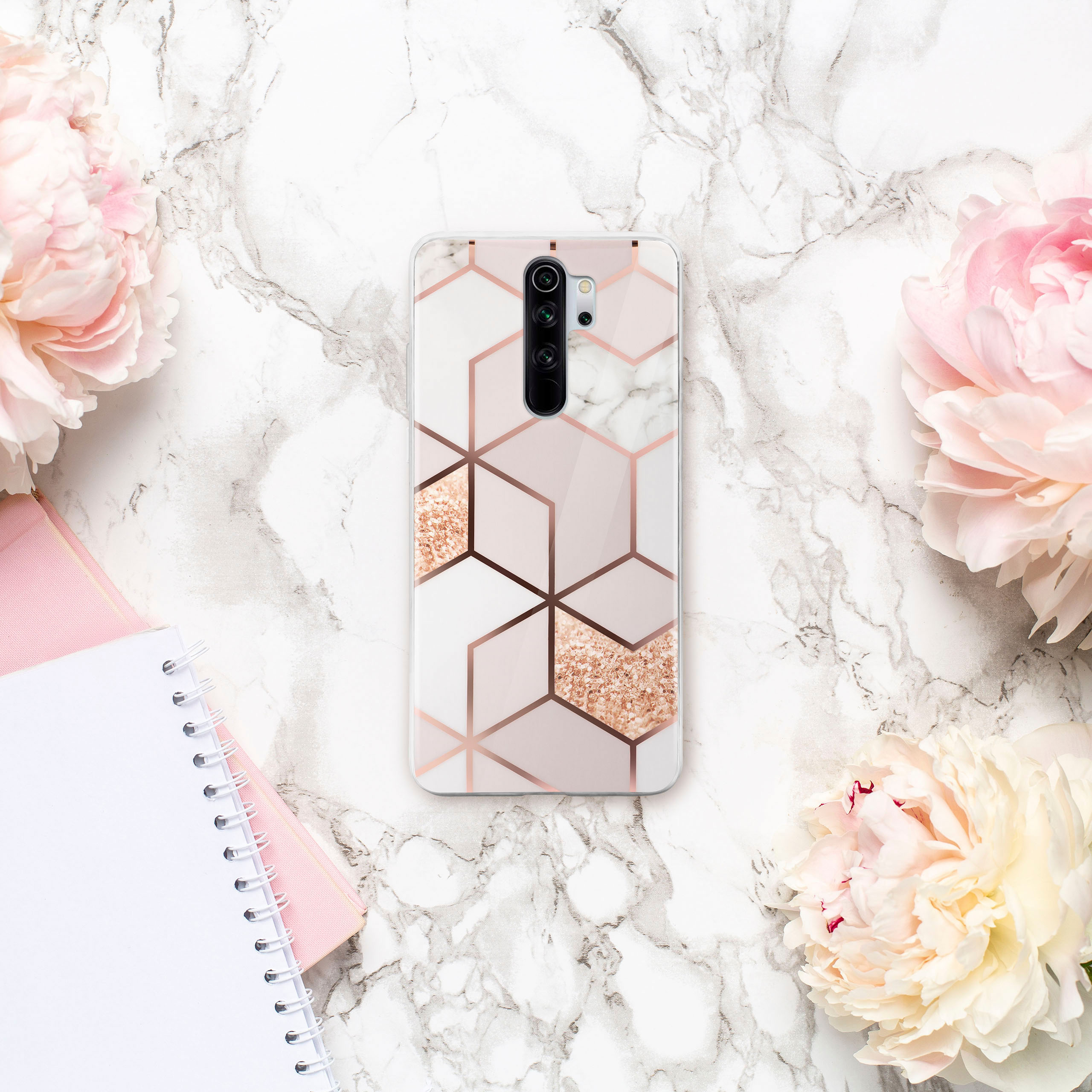 Handyhülle mit geometrischem Design auf Marmorhintergrund. Pinke Blumen im Hintergrund.