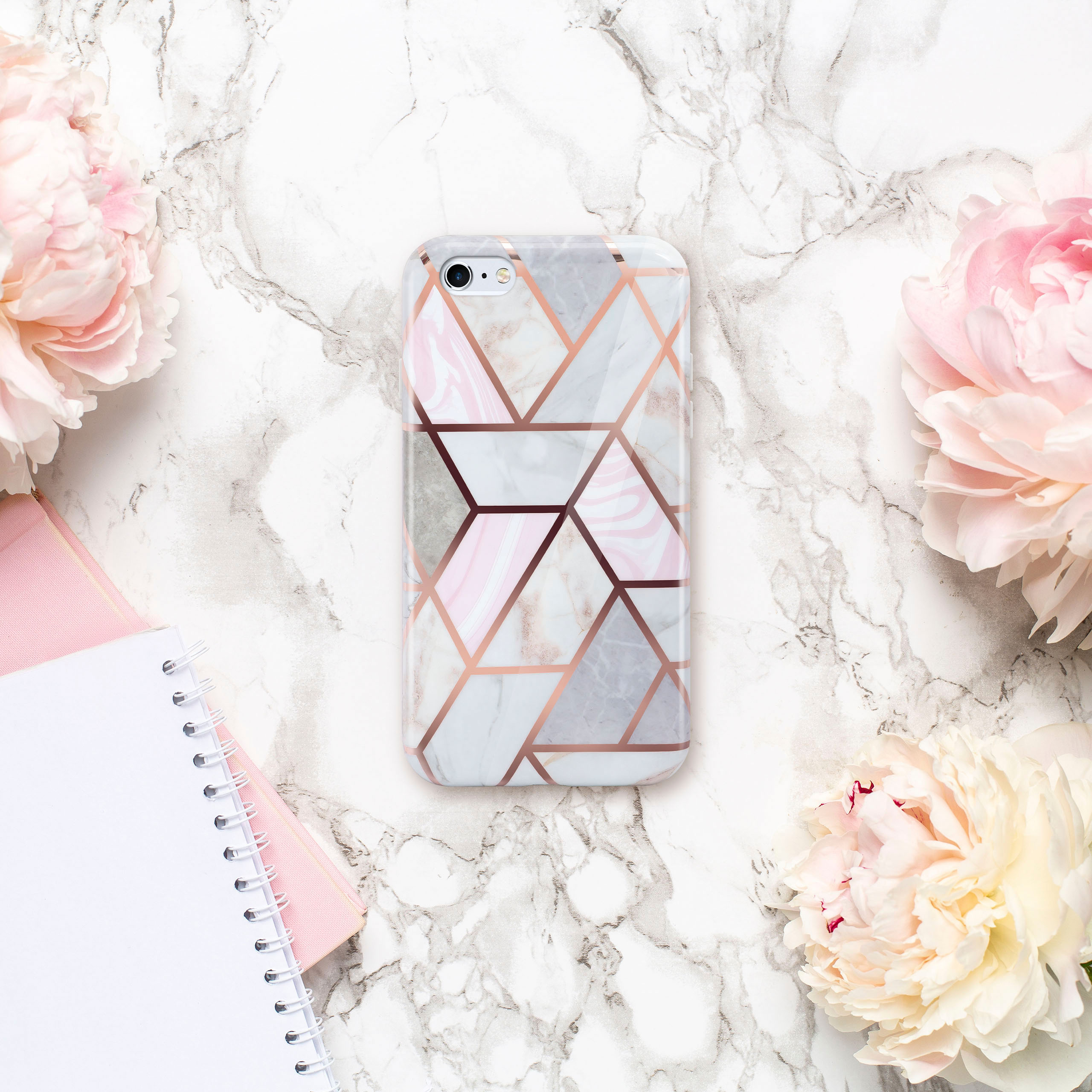 Handyhülle mit geometrischem Design und rosa Akzenten auf Marmor, umgeben von Blumen.