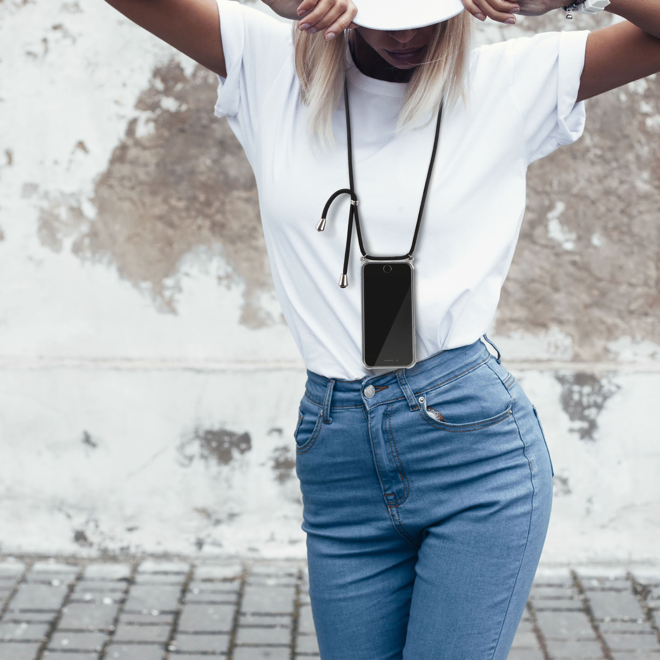 Eine Frau in einem weißen T-Shirt und Jeans, die eine Handyhülle mit Lanyard und einen weißen Hut trägt.