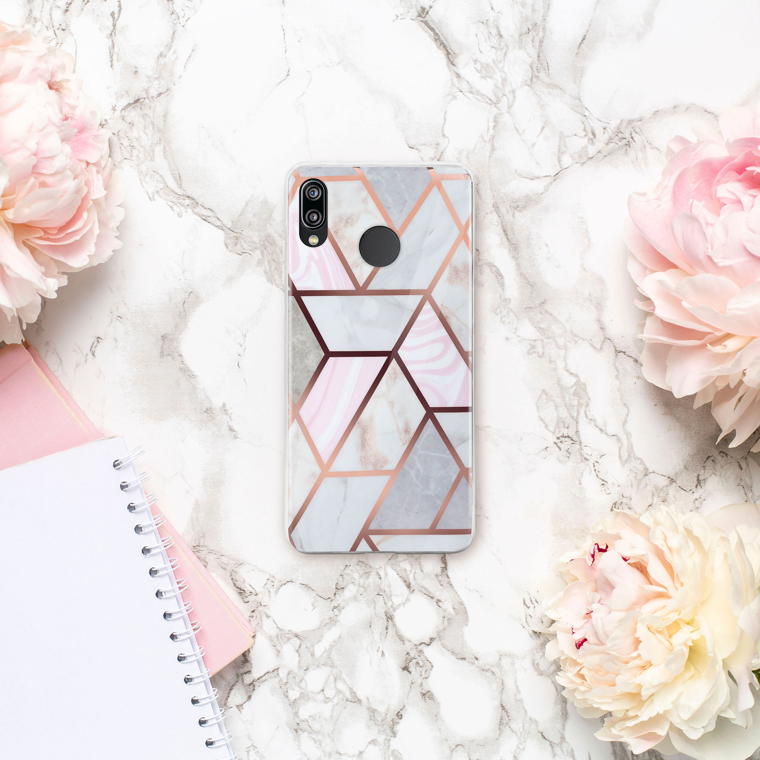 Handyhülle auf Marmor mit Blumen und Notizbuch. Hülle hat rosa und weißes geometrisches Muster.