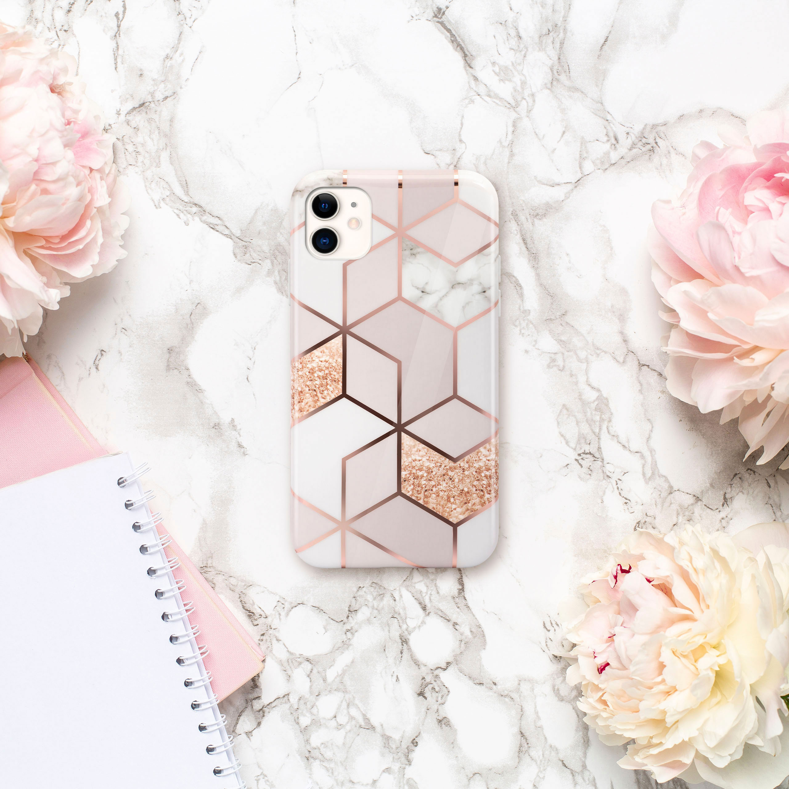 Eine Handyhülle auf Marmor mit Blumen und Notizbuch. Hülle hat geometrisches Design.