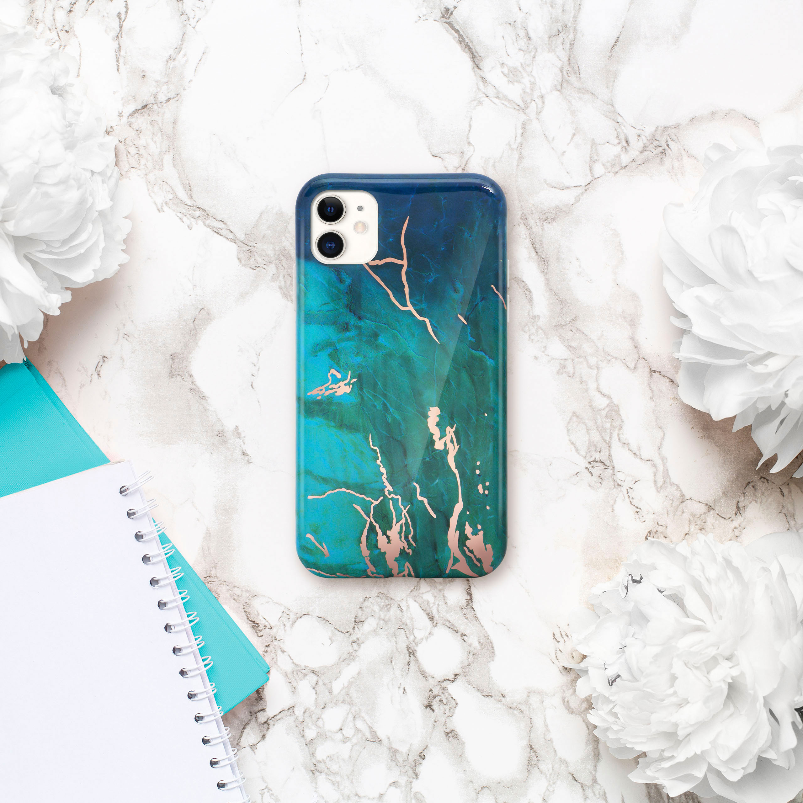 Handyhülle mit blauem und grünem Marmordesign, umgeben von weißen Blumen und einem Notizbuch.