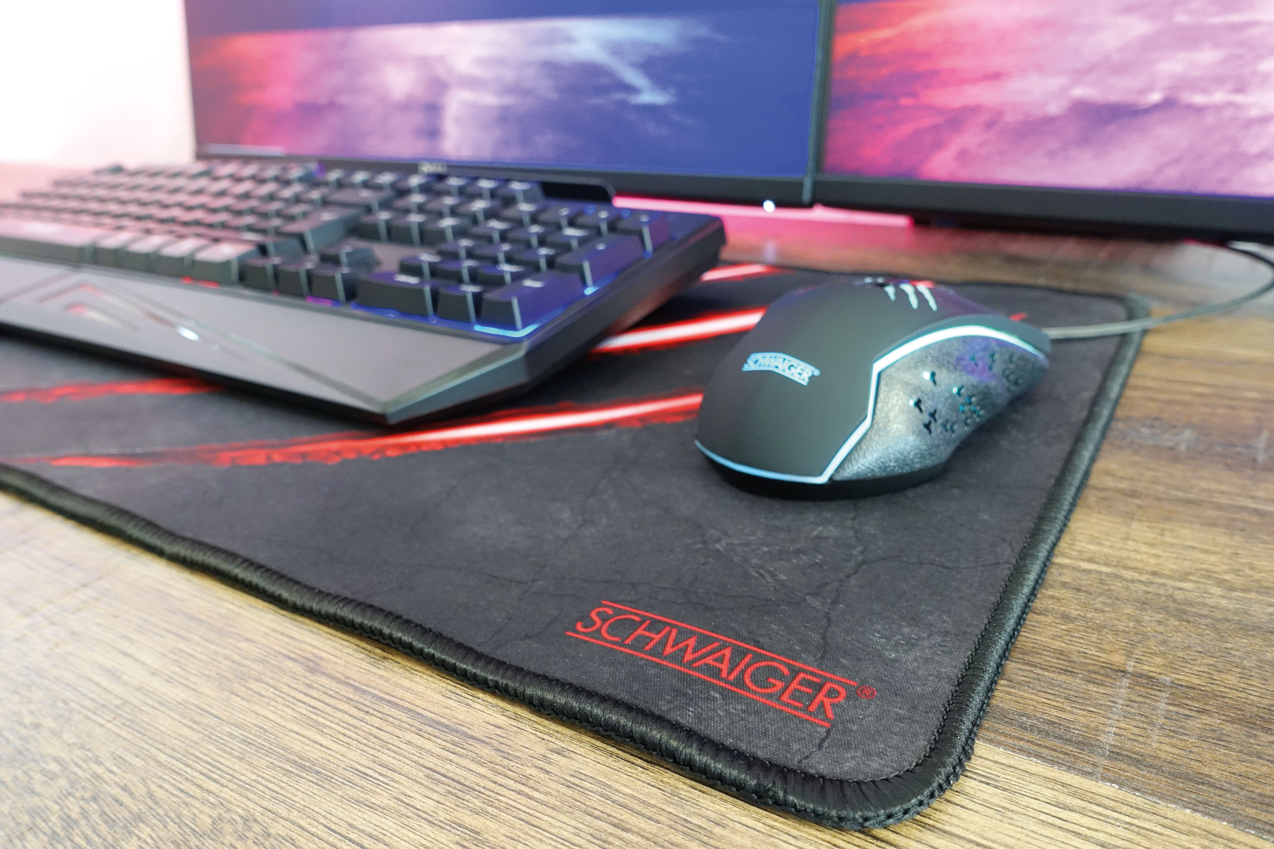 Gaming-Setup mit Tastatur, Maus und Mauspad. Rote und blaue Lichter. Holztisch.