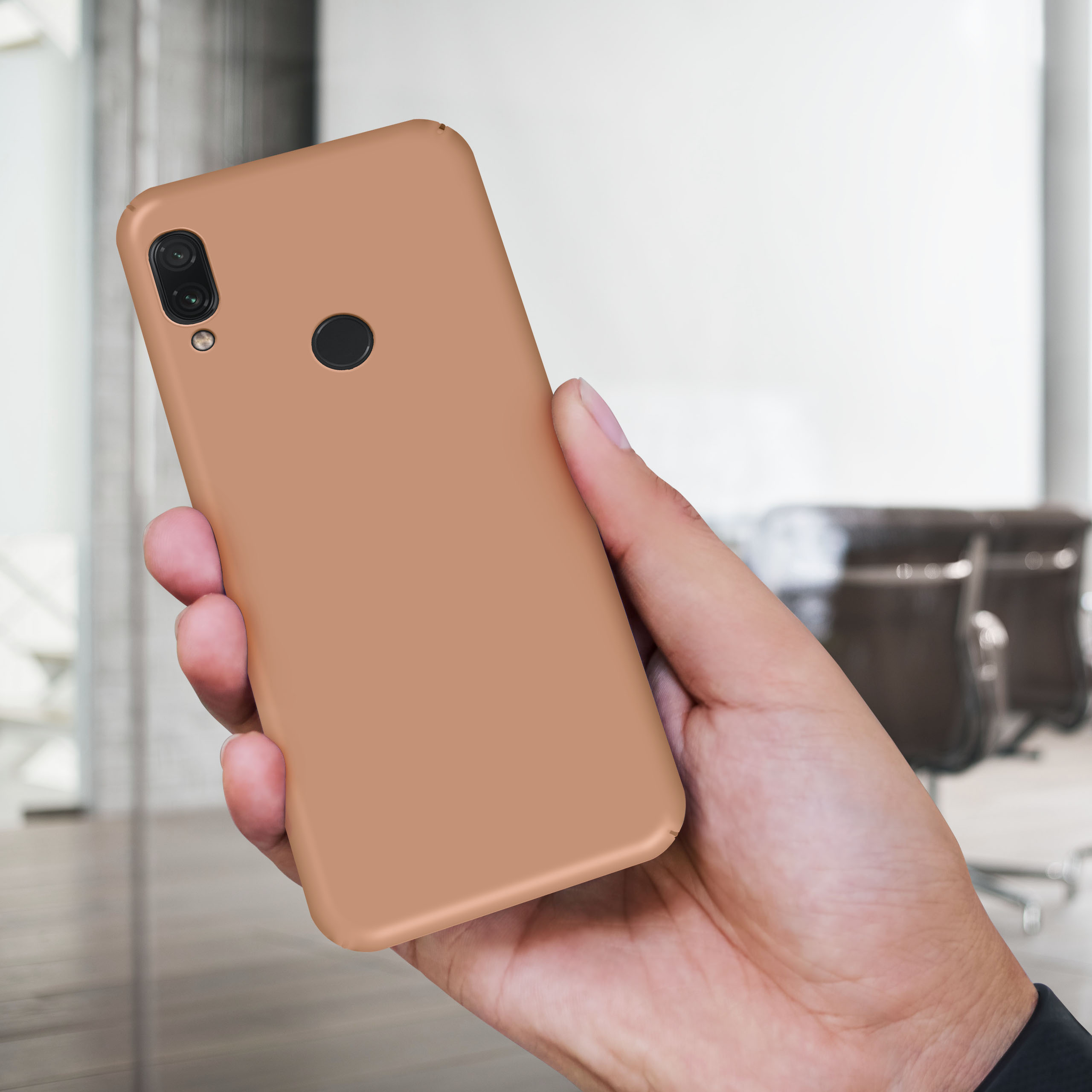 Hand hält ein beiges Telefon. Hintergrund ist ein verschwommenes Büro mit Stühlen.