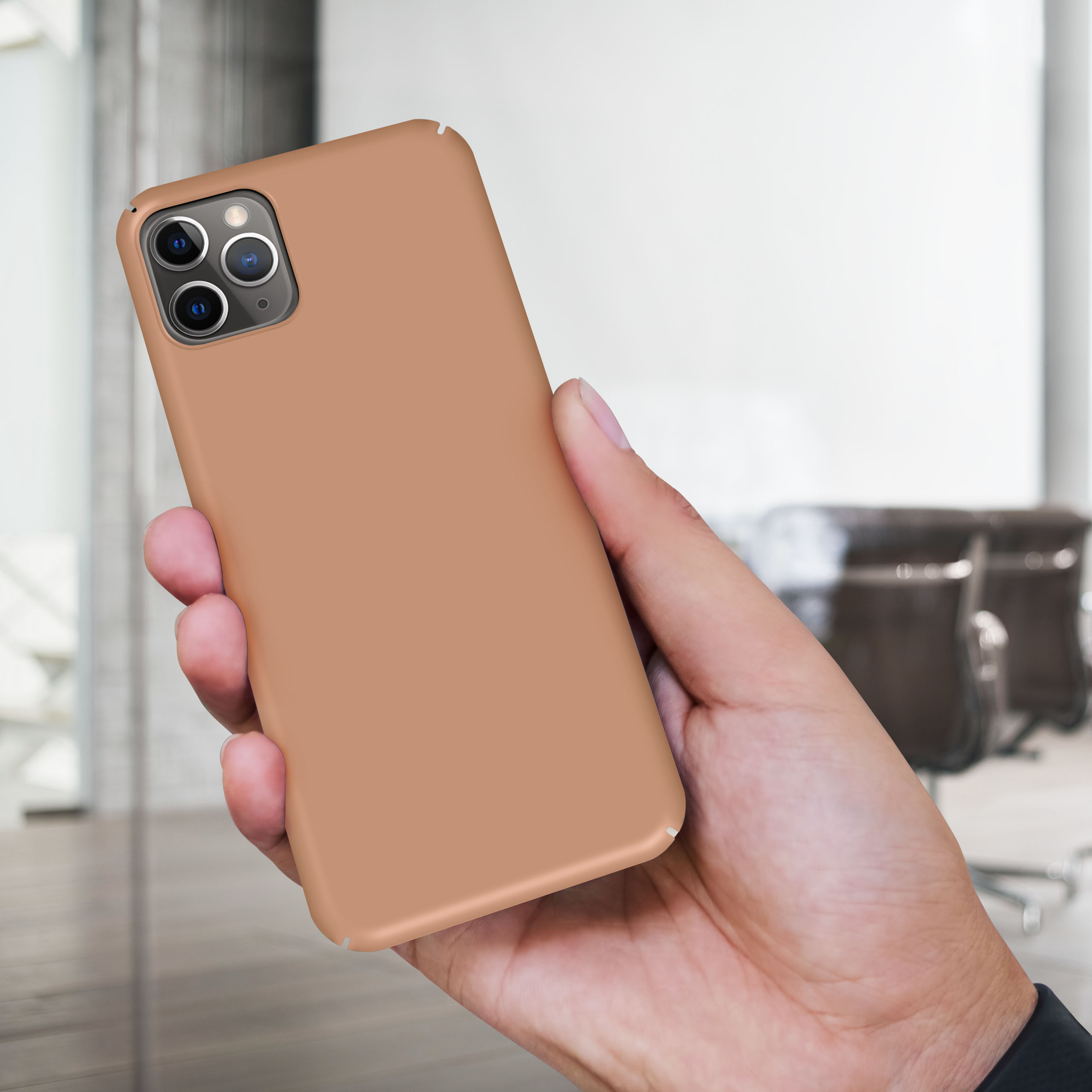 Hand, die ein Telefon mit brauner Hülle hält, in einem Raum.