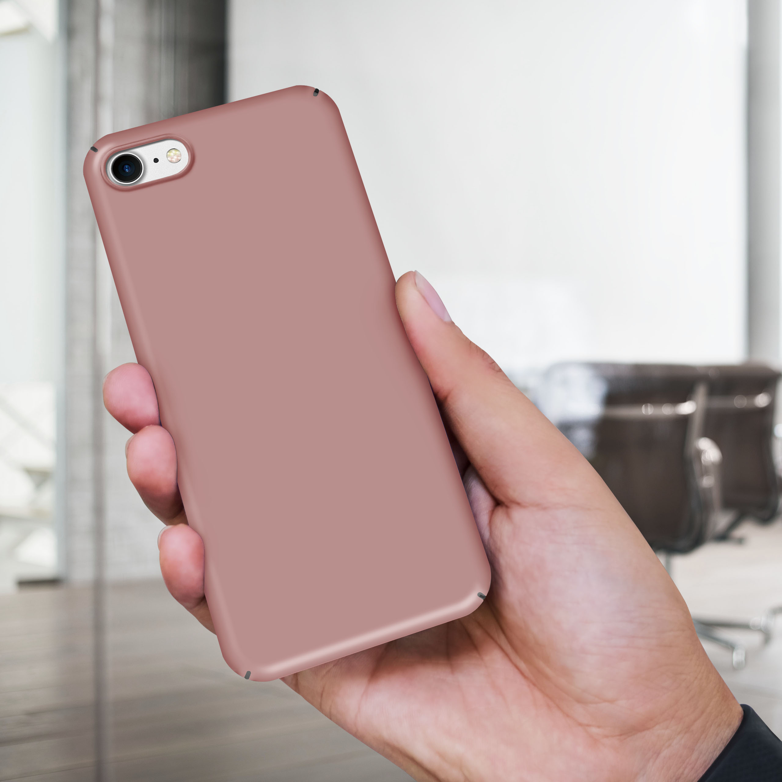 Eine Hand hält eine rosa Handyhülle. Der Hintergrund zeigt ein verschwommenes Büro- oder Wohninterieur.