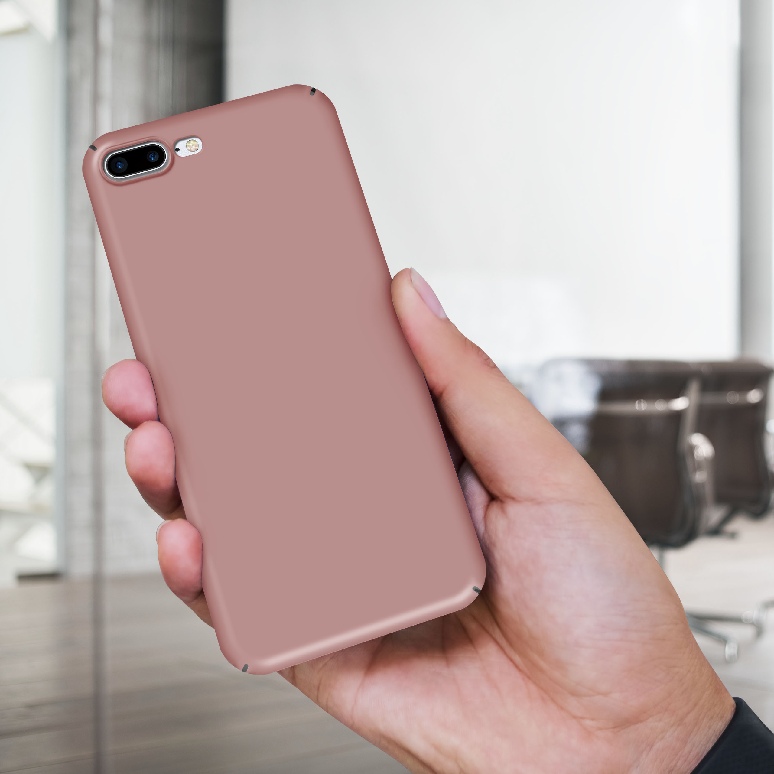 Eine Hand hält ein roségoldenes Telefon. Der Hintergrund ist verschwommen, mit Bürostühlen und einer weißen Wand.