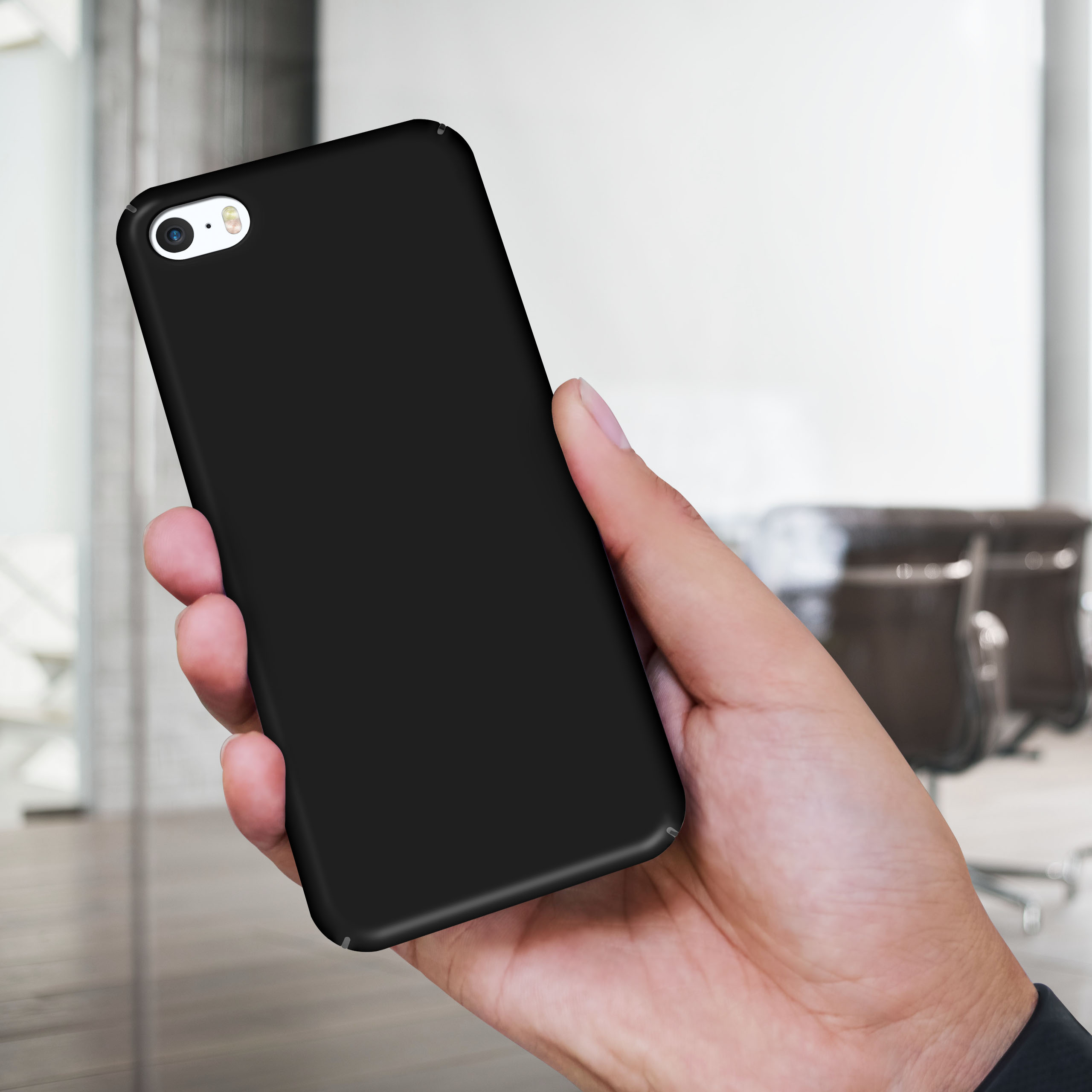 Hand hält ein schwarzes Telefon, die Kamera ist sichtbar. Verschwommenes Büro im Hintergrund.