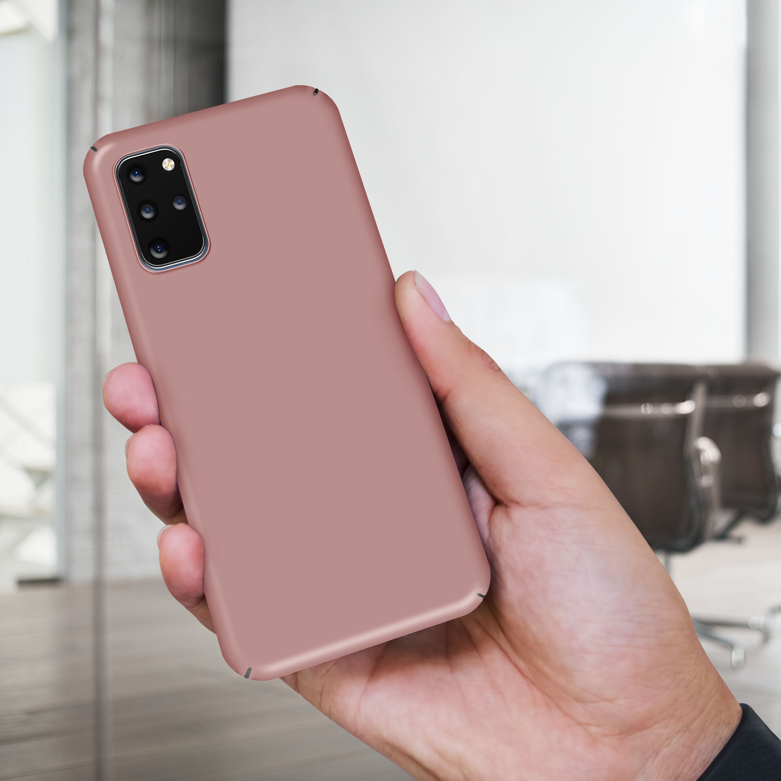 Hand hält rosafarbenes Telefon. Verschwommener Bürohintergrund. Telefonrückseite sichtbar. Schlichtes Design.