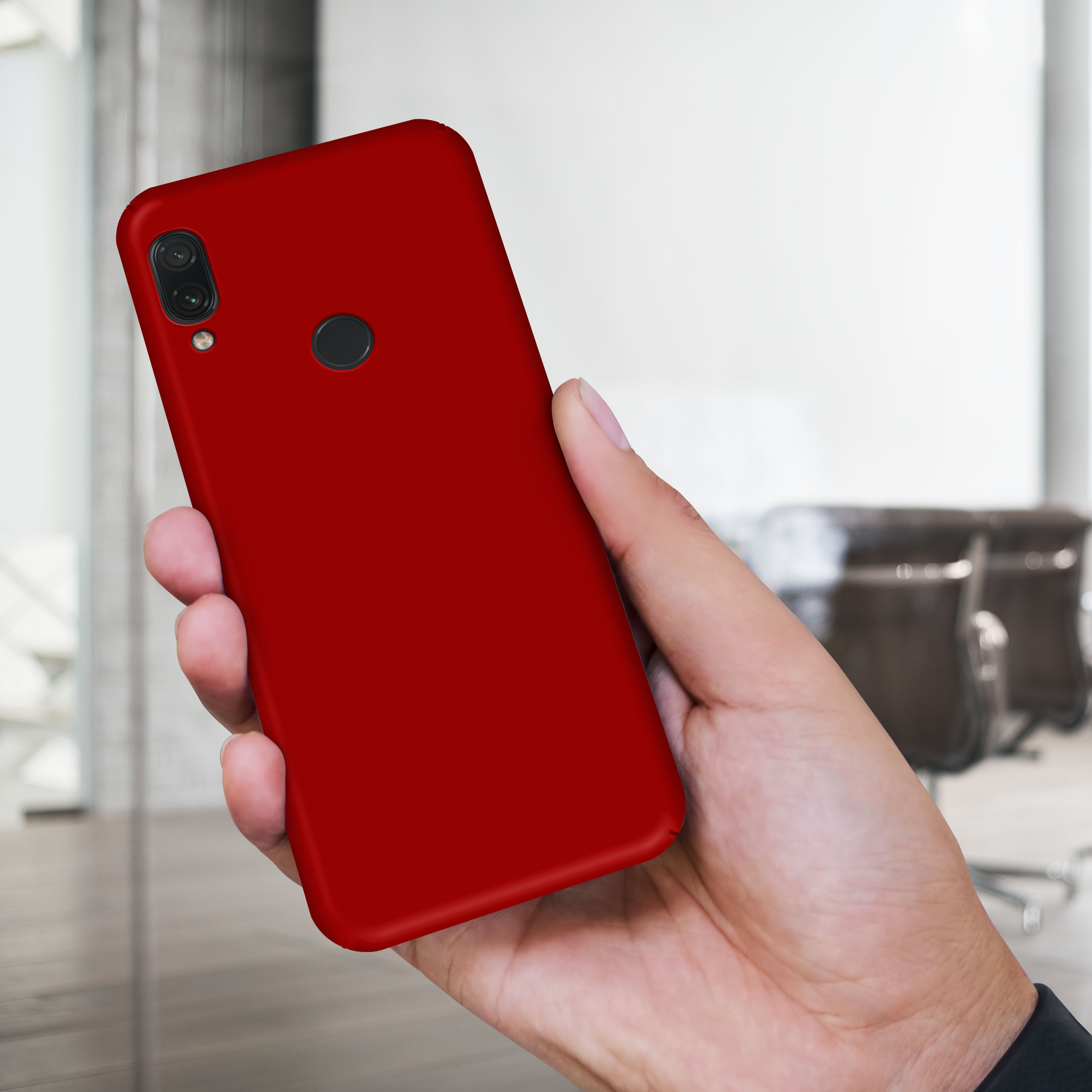 Eine Hand hält eine rote Handyhülle. Verschwommene Bürostühle sind im Hintergrund.
