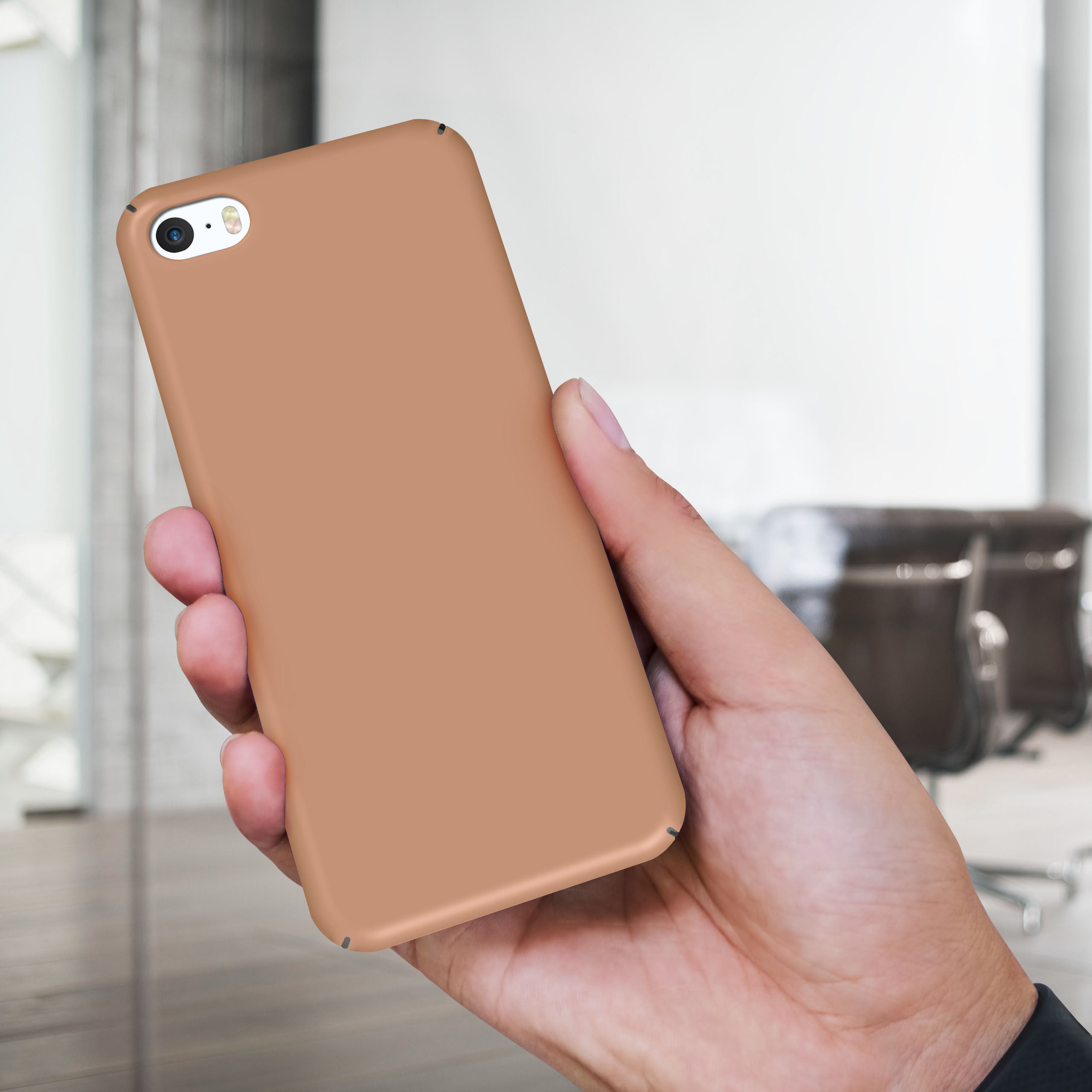Hand hält ein Telefon mit brauner Hülle. Der Hintergrund ist ein verschwommenes Büroumfeld.
