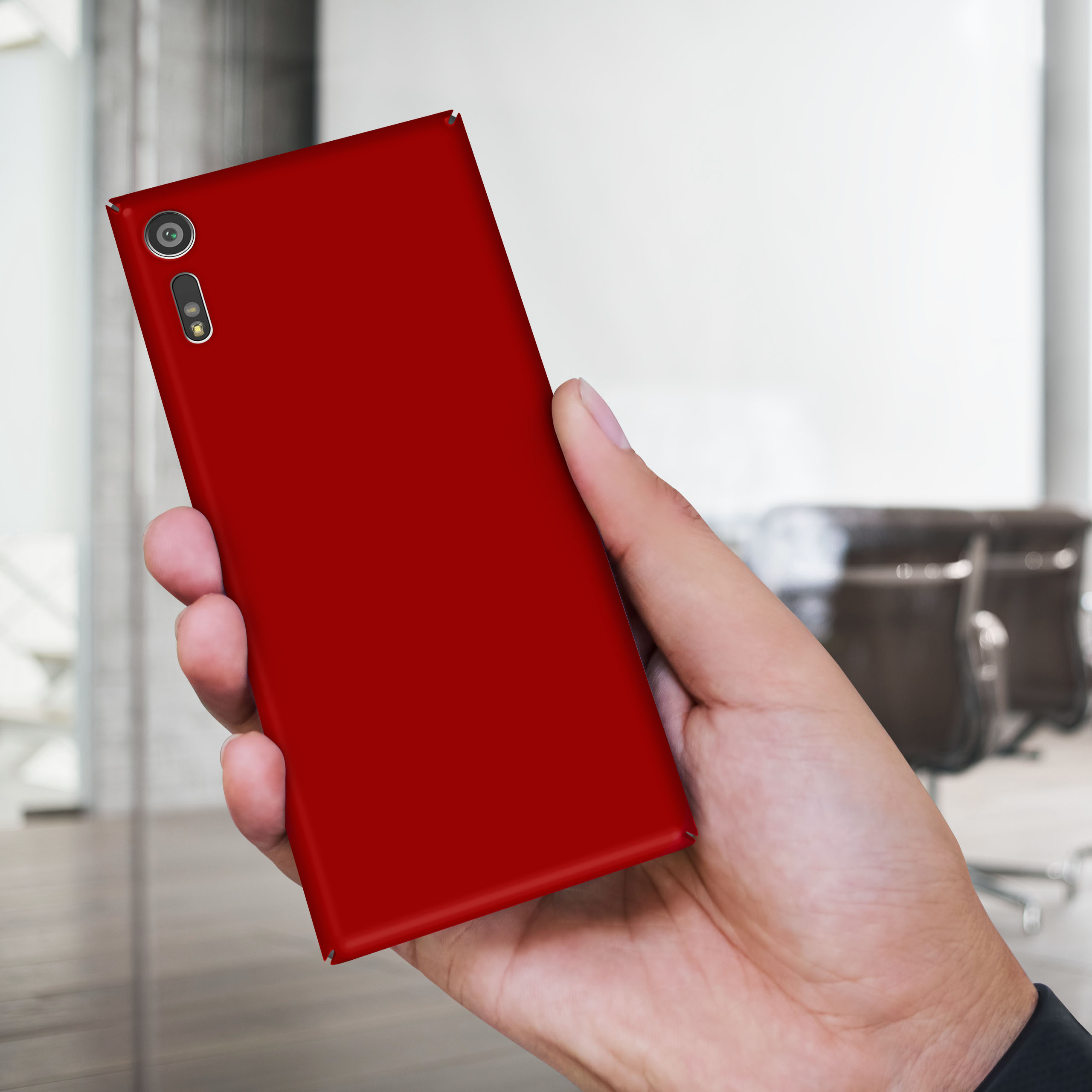 Hand hält rotes Smartphone, Rückseite mit Kamera und Blitzlicht, in Büroumgebung.