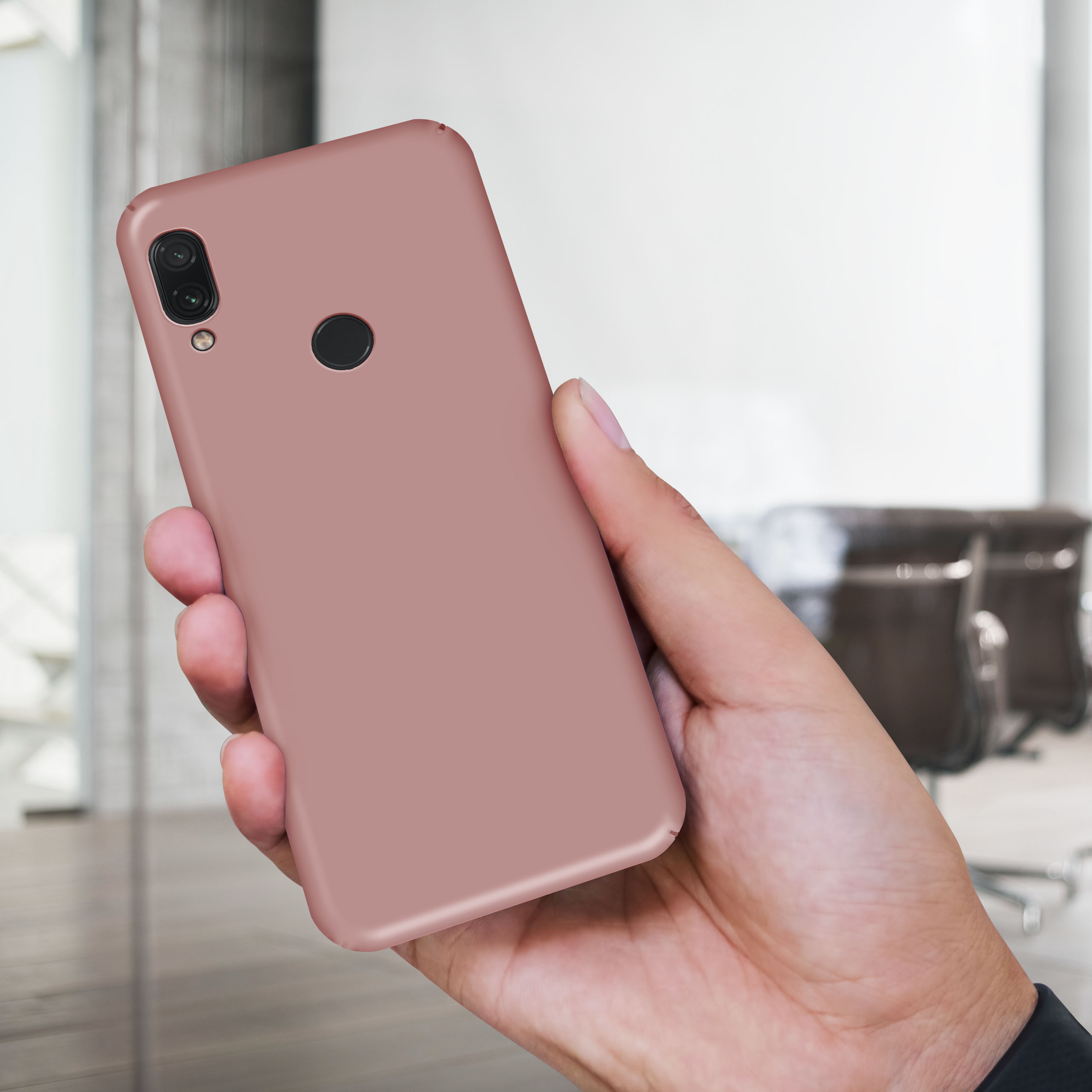 Hand hält Telefon mit rosa Hülle vor verschwommenem Büro.