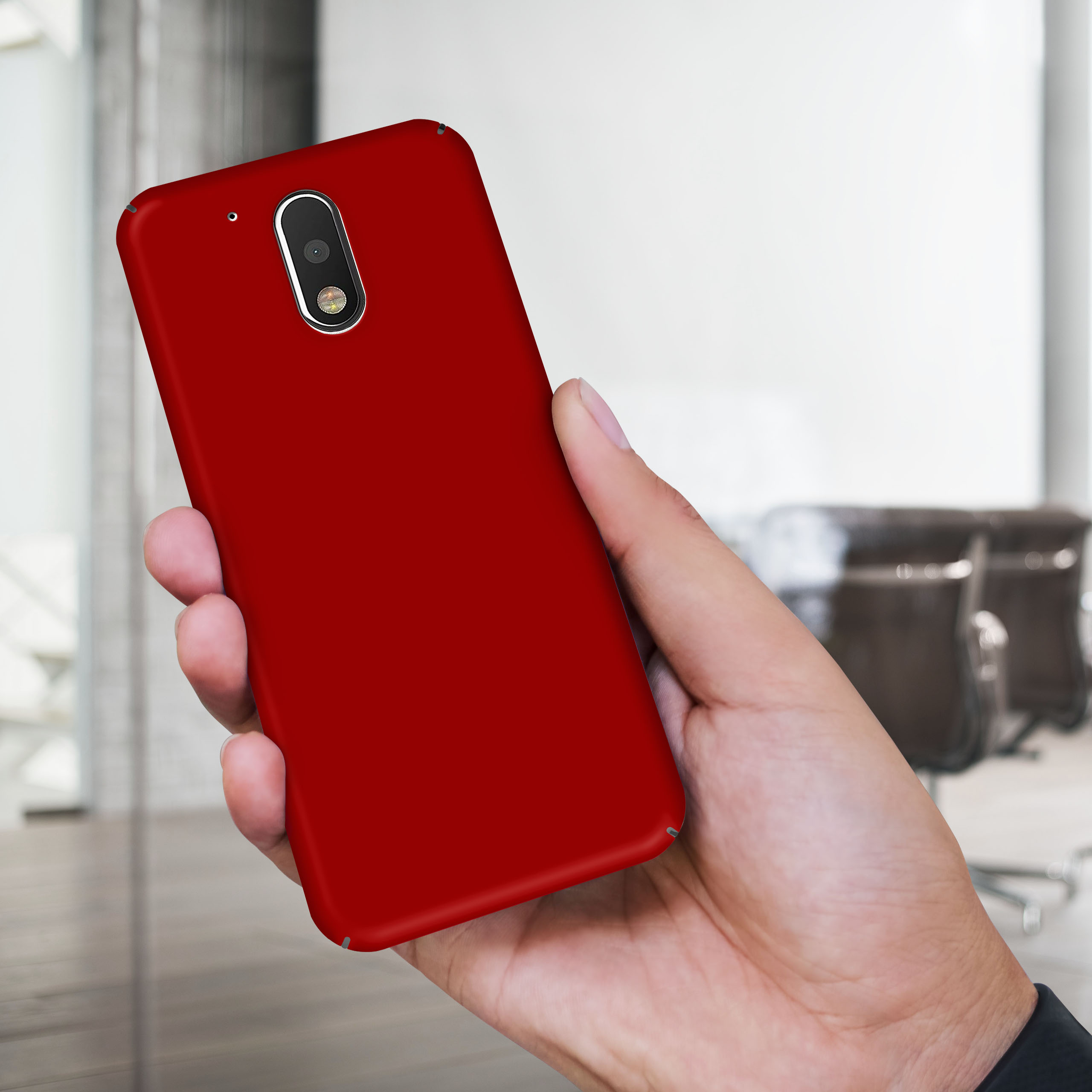 Eine Hand, die eine rote Handyhülle hält. Der Hintergrund ist verschwommen und zeigt Stühle und eine Wand.