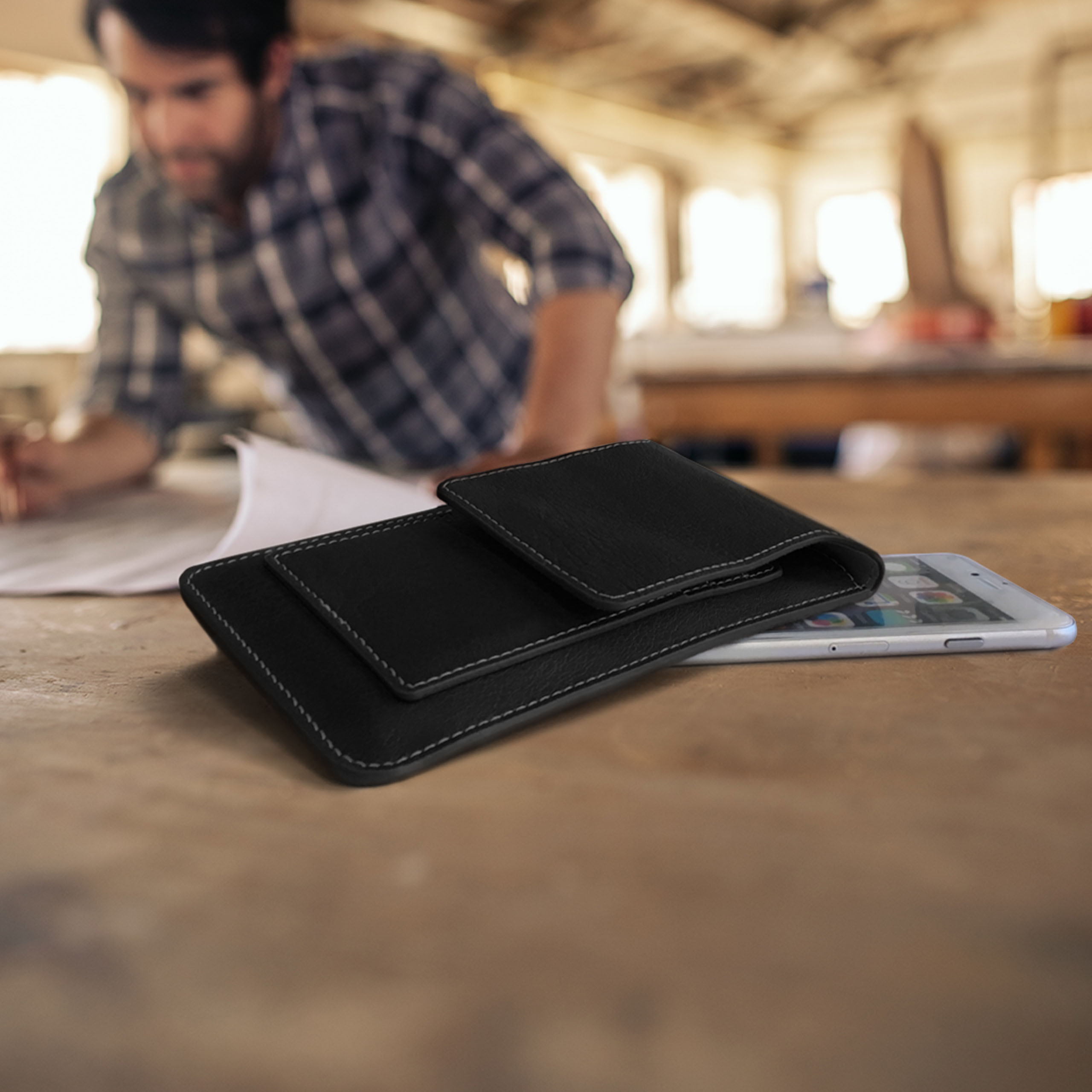 Person arbeitet an Papier auf Holztisch, daneben Handyhülle und Handy.