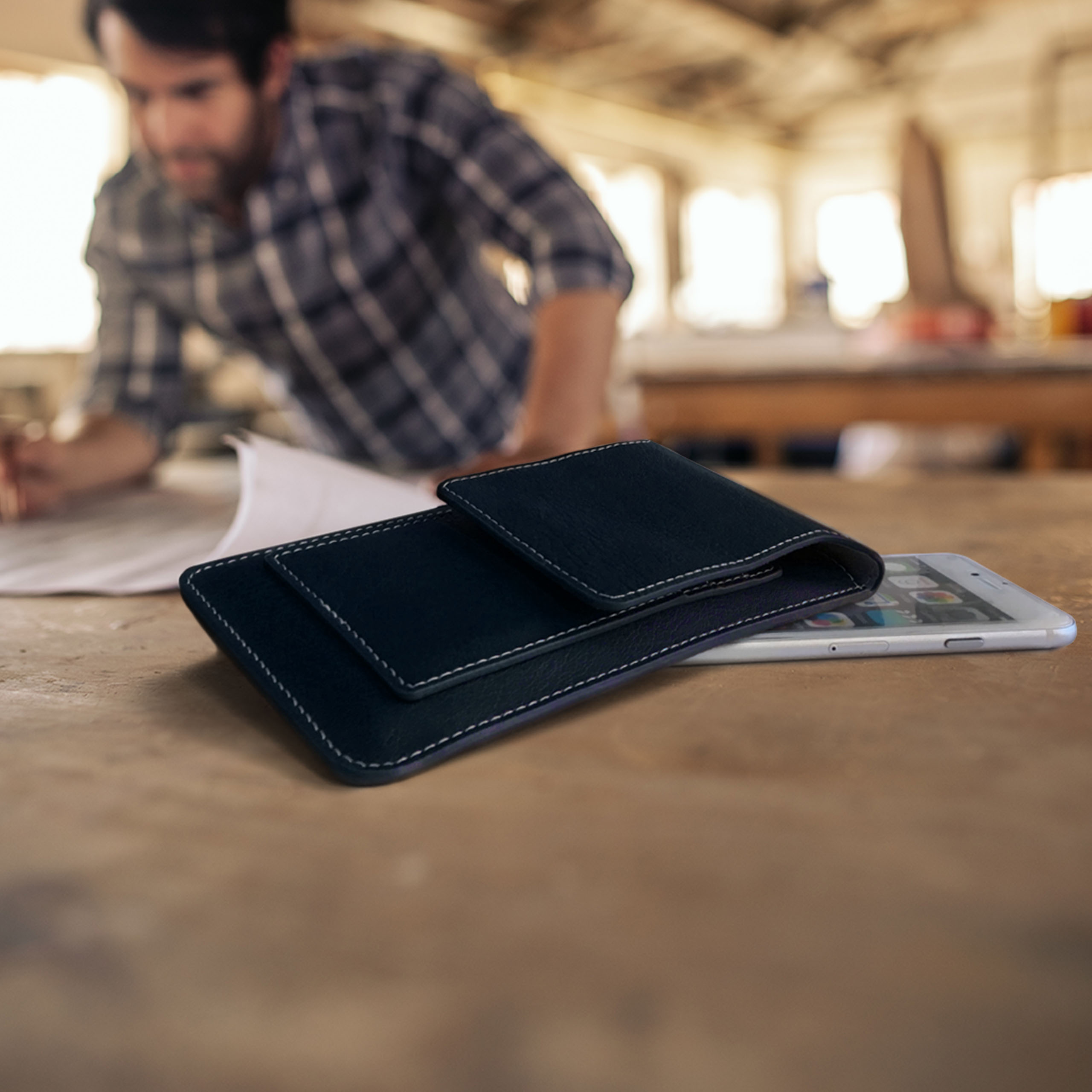 Person arbeitet an Papier auf Holztisch, daneben Handyhülle und Handy.
