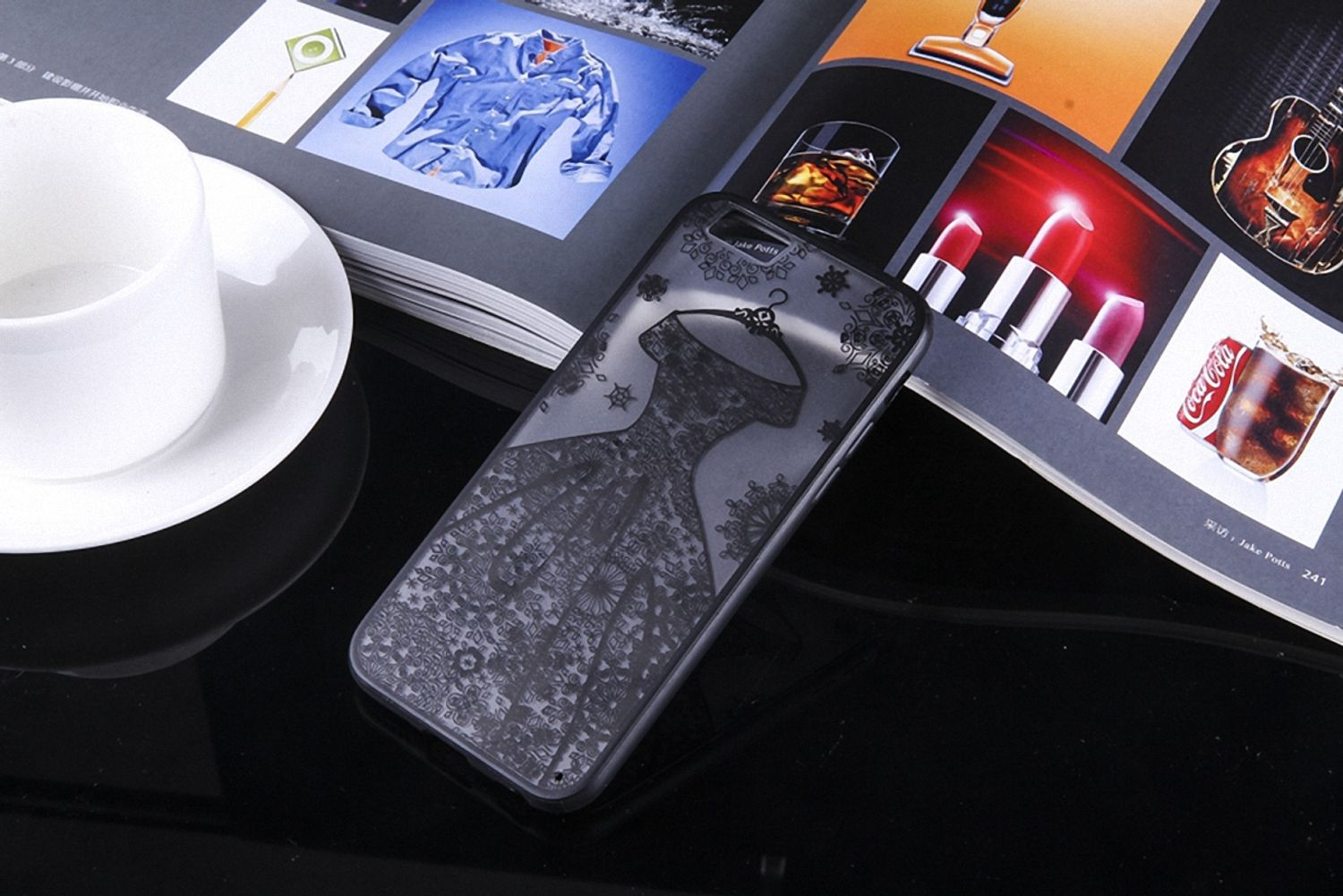 Smartphone-Hülle mit Kleid-Design auf glänzender Oberfläche, mit Magazin und anderen Gegenständen im Hintergrund.