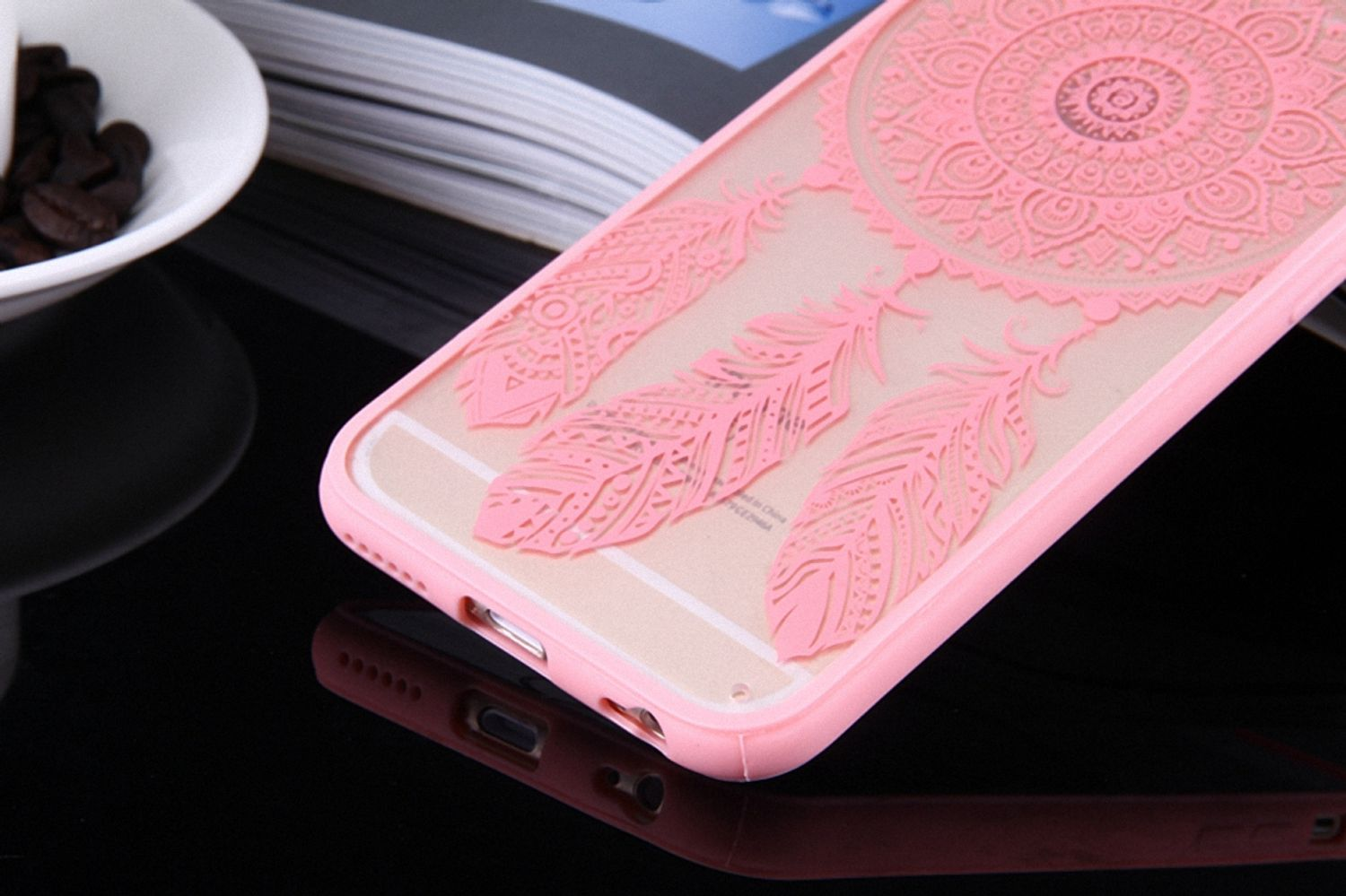 Rosa Handyhülle mit Traumfänger-Design. Kaffeebohnen im Hintergrund. Das Telefon spiegelt sich.