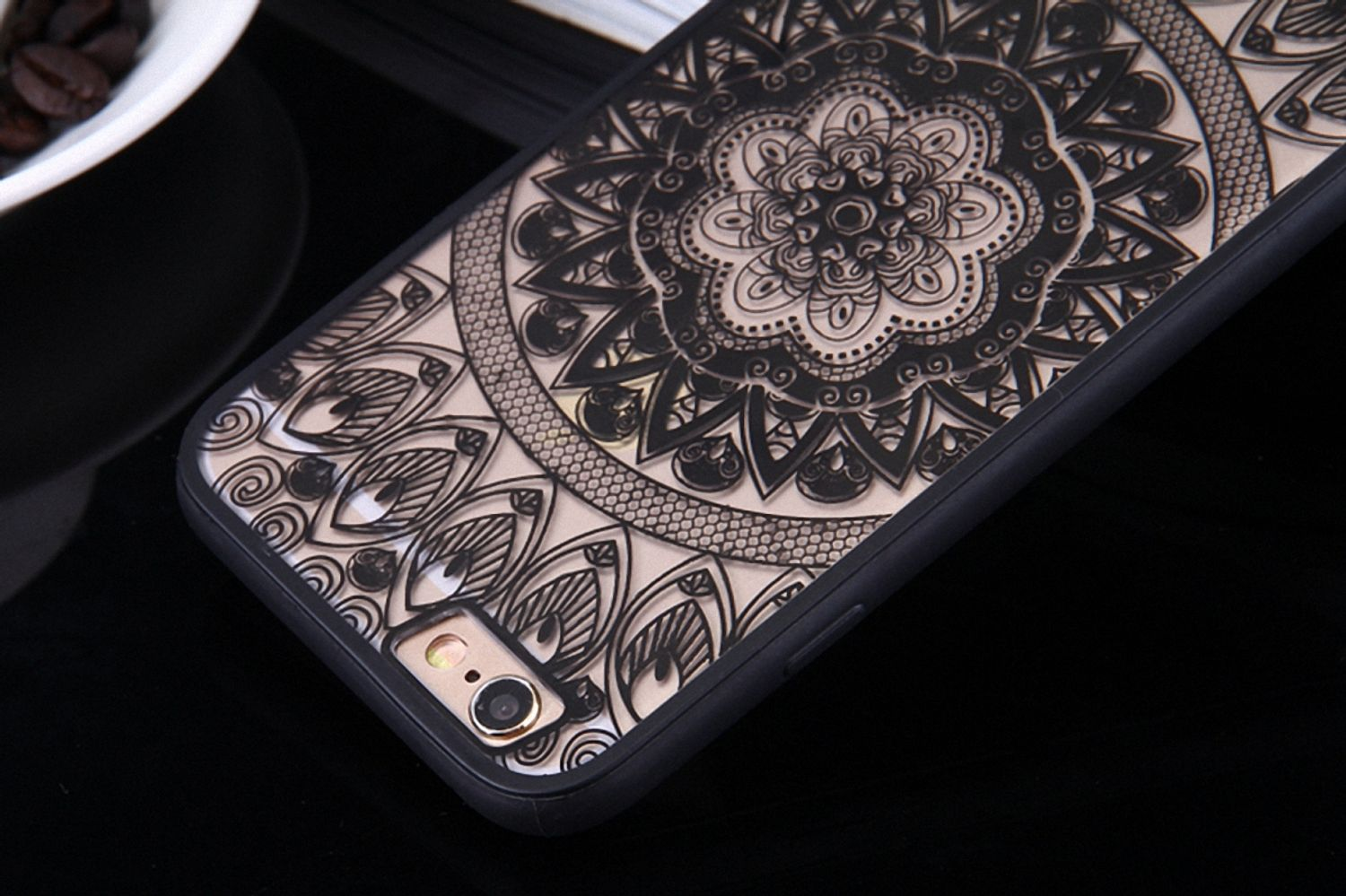 Eine Handyhülle mit einem schwarzen und beigen Mandala-Design. Die Hülle liegt auf einer schwarzen Oberfläche.