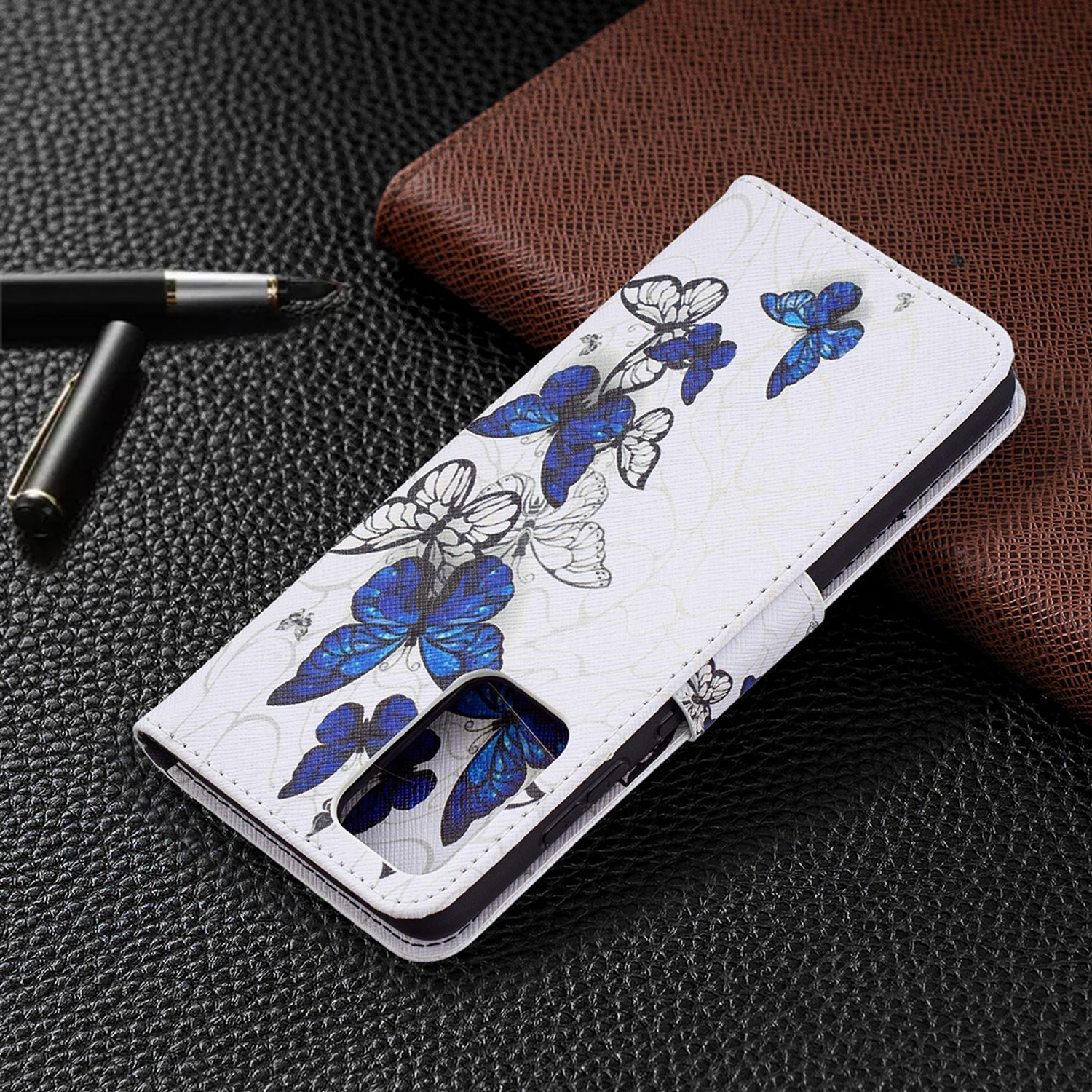Weiße Handyhülle mit blauem Schmetterlingsdesign, offen, um das Telefon freizugeben. Es liegt auf einer schwarzen Lederoberfläche.