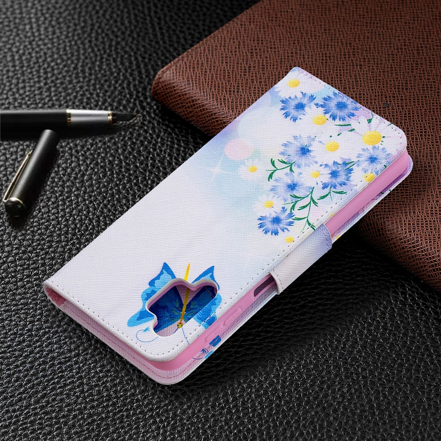 Weiße Handyhülle mit Blumen- und Schmetterlingsdesign, auf dunkler Oberfläche neben Stift.