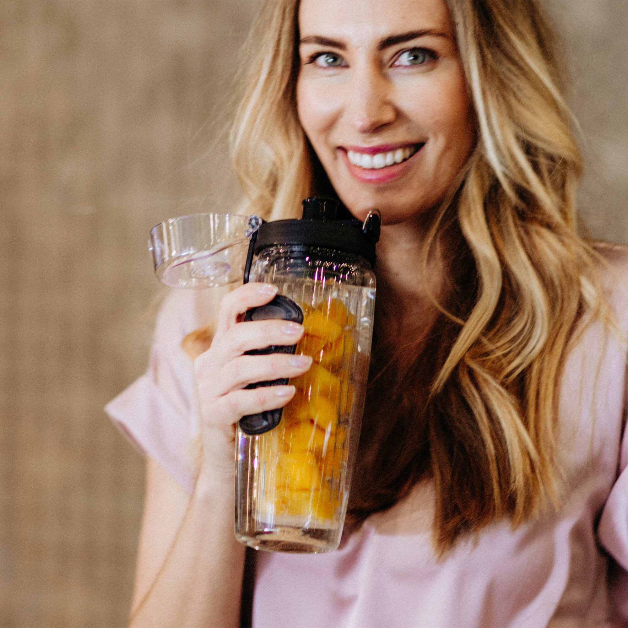 Eine Frau hält eine transparente Flasche mit Orangenscheiben darin, lächelnd.