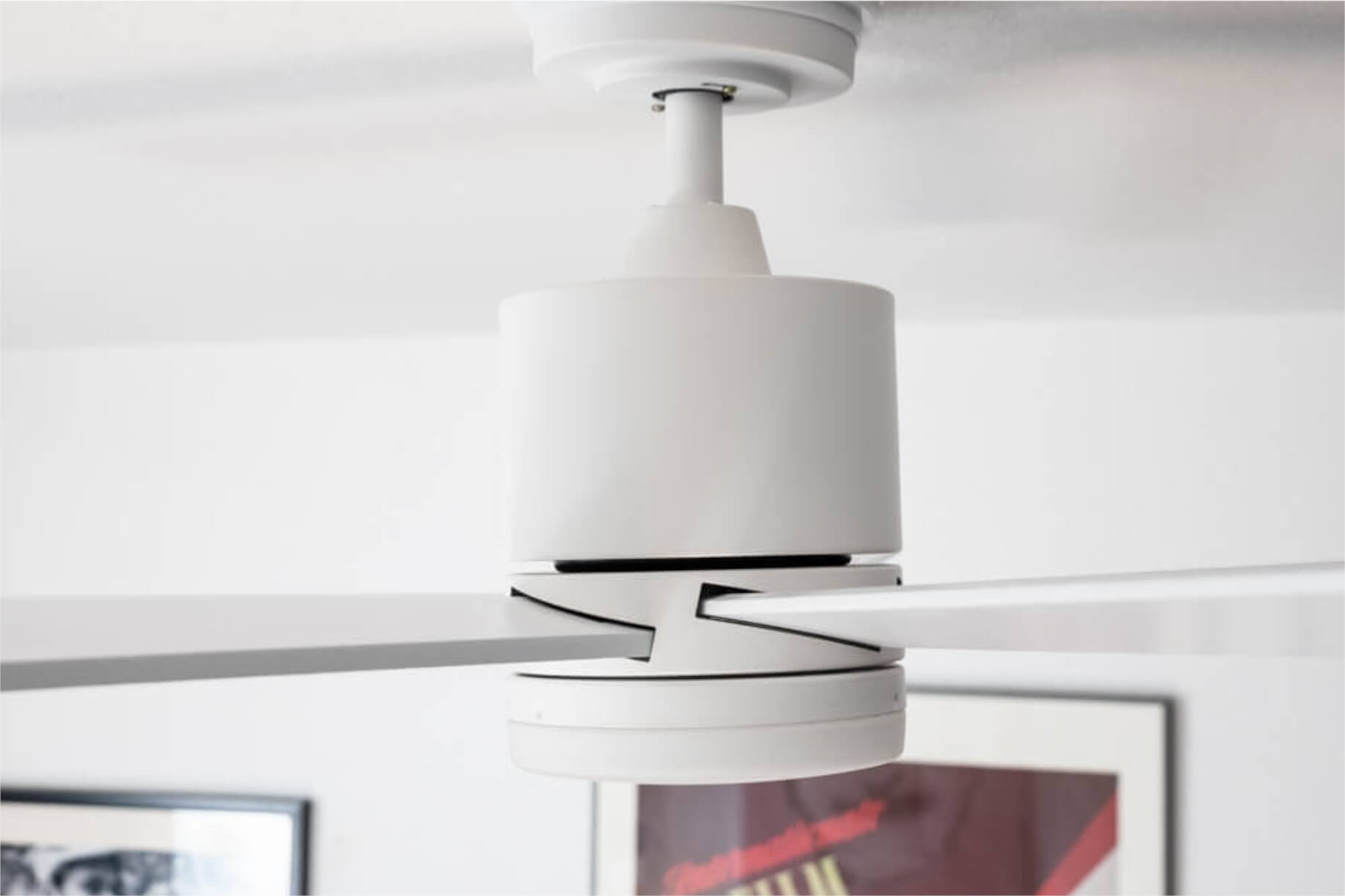 Ein weißer Deckenventilator mit drei Blättern. Einige Hintergrundbilder sind sichtbar.