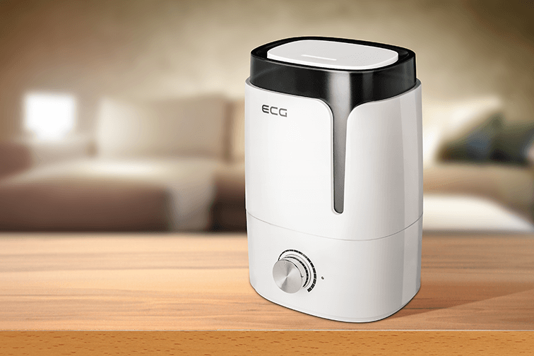 Biały nawilżacz na drewnianym stole, rozmyte tło sypialni.