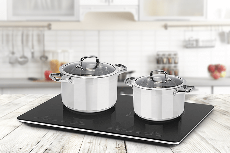 Dwa garnki ze stali nierdzewnej ze szklanymi pokrywkami na czarnej płycie indukcyjnej.