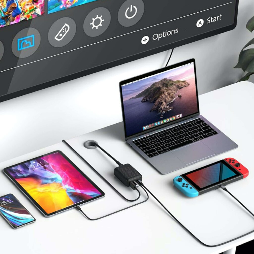 Weißer Schreibtisch mit Laptop, Tablet, Telefon und Nintendo Switch, alle mit einem schwarzen Hub verbunden.