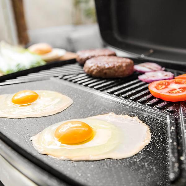 Una parrilla con huevos fritos, hamburguesas, tomates y cebollas rojas. Cocinando en una parrilla negra.