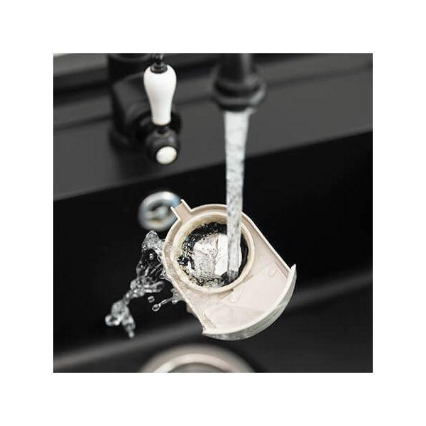 Wasser, das in ein Waschbecken fließt und einen weißen, offenen Filter mit schwarzen Rückständen wäscht.
