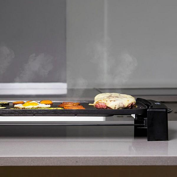 Una piastra elettrica piatta con cibo. Il cibo alla griglia comprende verdure a fette e un hamburger con formaggio fuso.